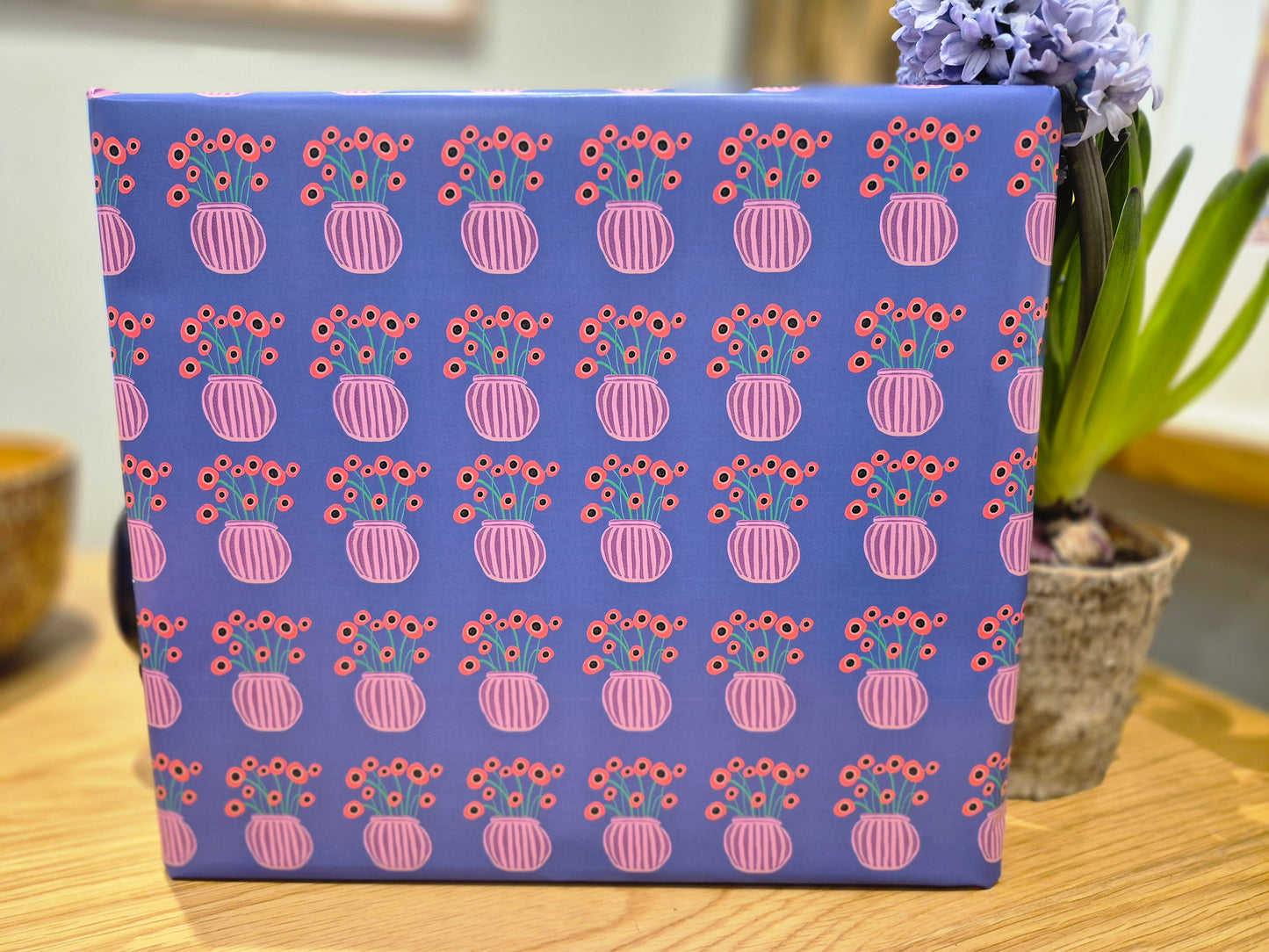 Blue botanical wrapping paper featuring a hand illustrated flower vase design with a striped vase and red poppies