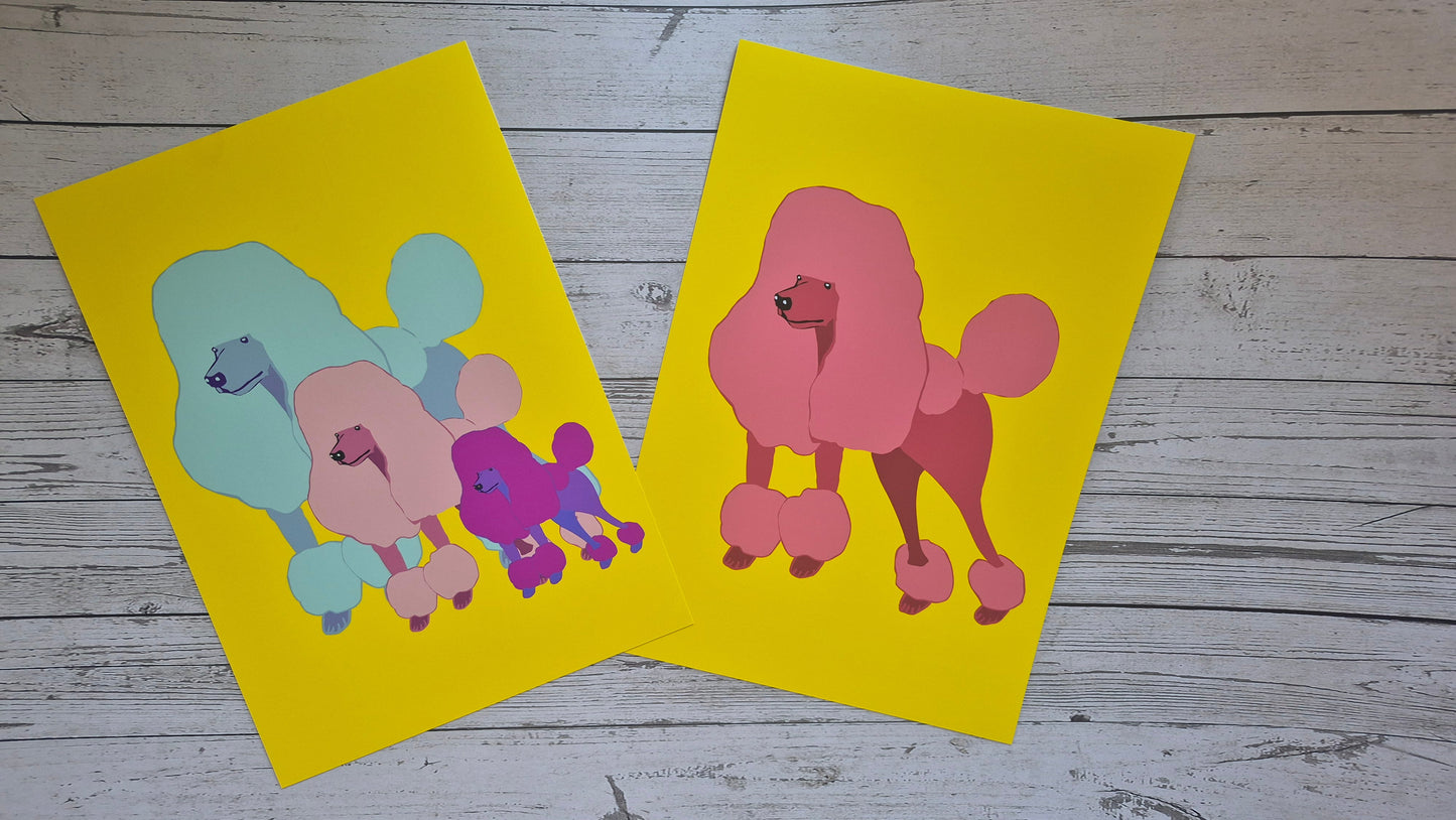 Two colourful poodle illustrations printed on yellow fine art paper against a wooden surface.
