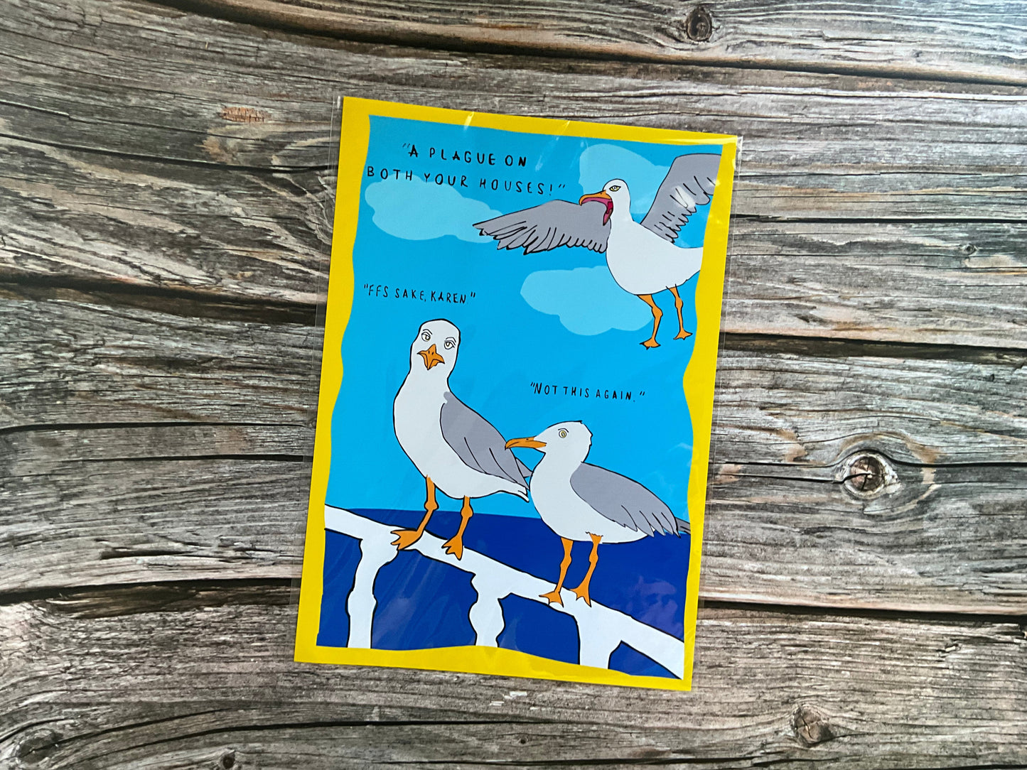 Funny seagull art print with yellow border on a wooden surface