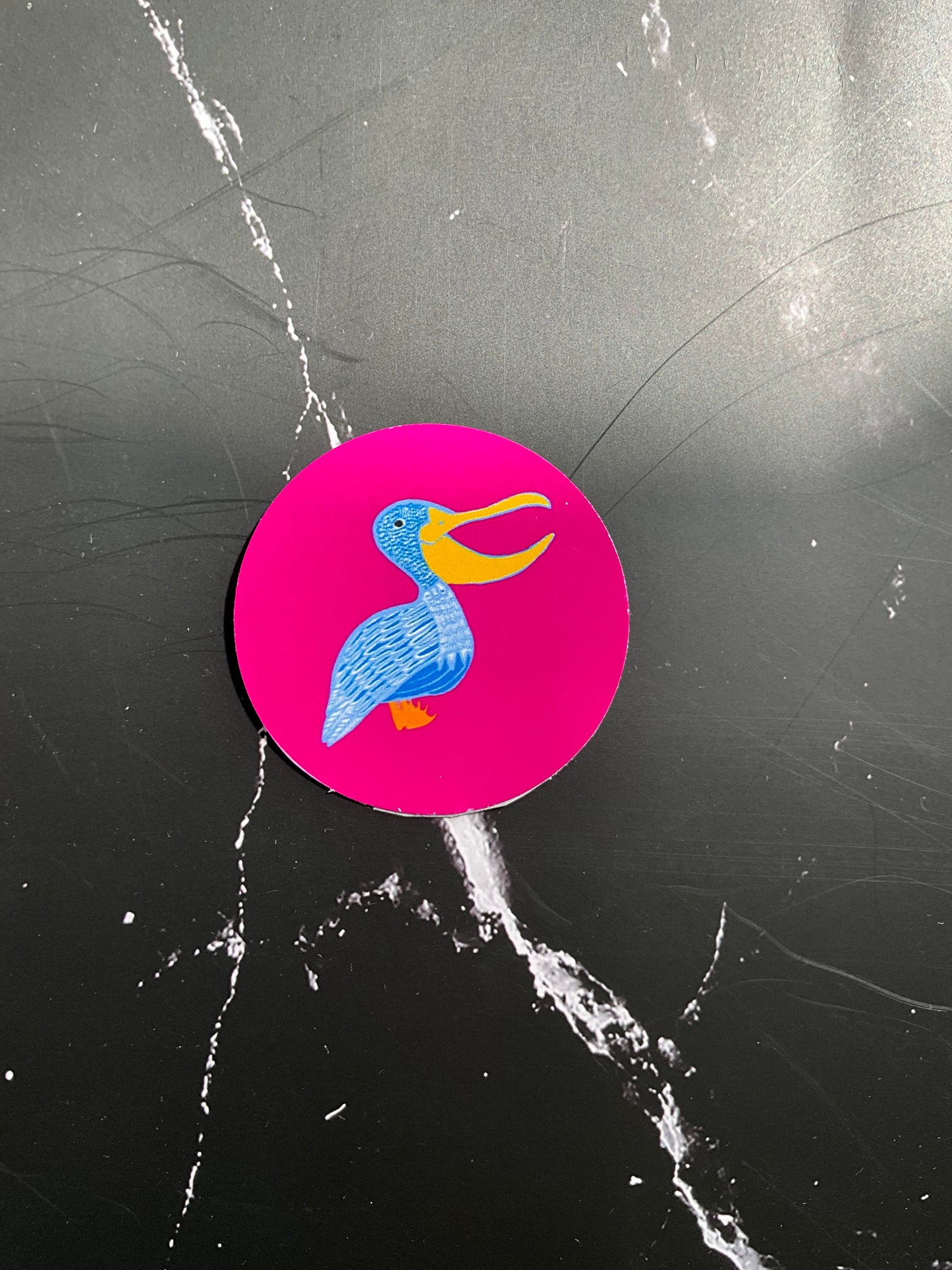 Circular sticker with a colourful pelican design on a black marble streaked surface