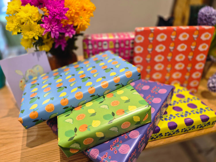 A pile of brightly wrapped presents on a table with flowers