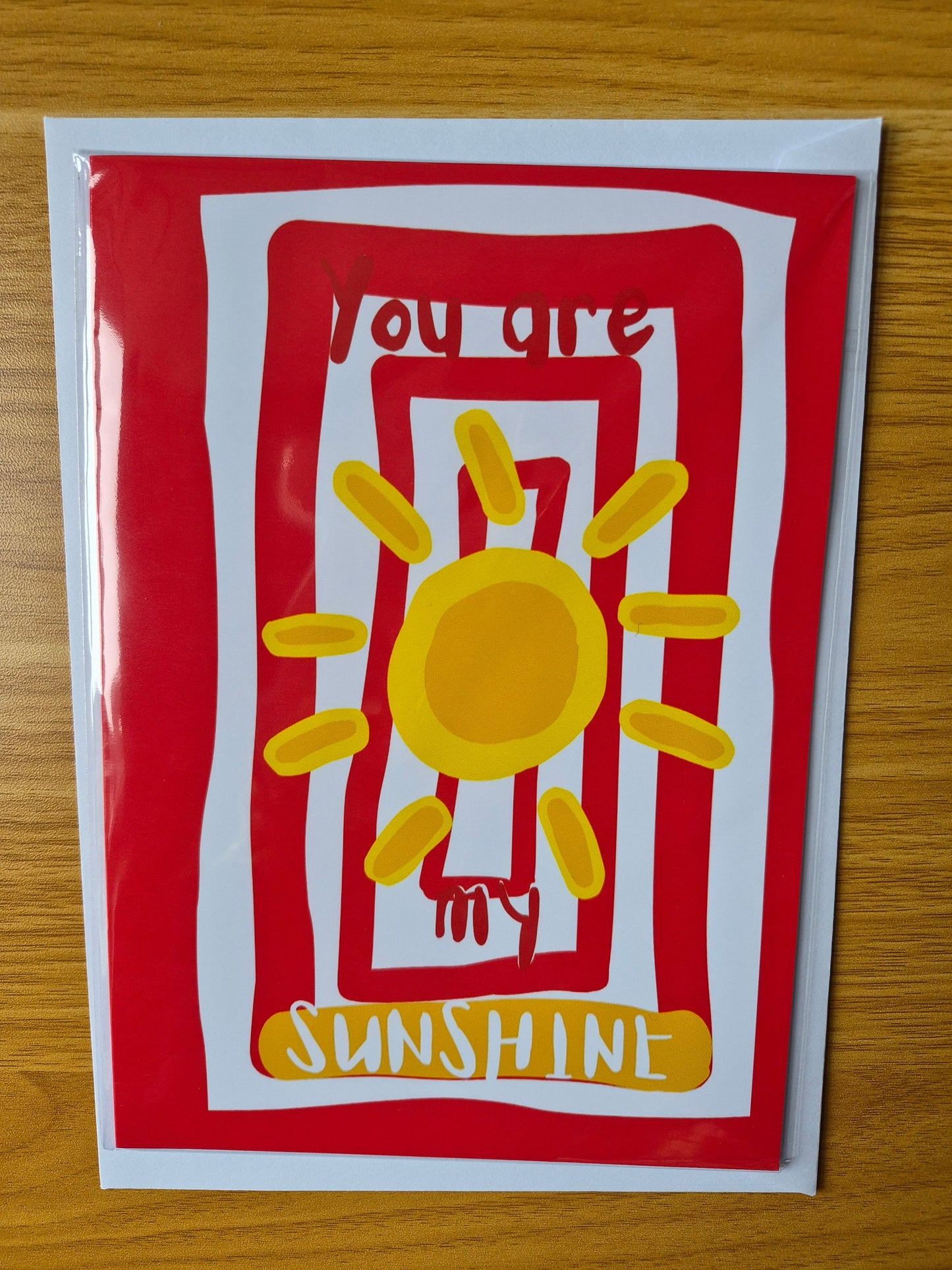 Card with a yellow sun design and red striped border on a wooden surface