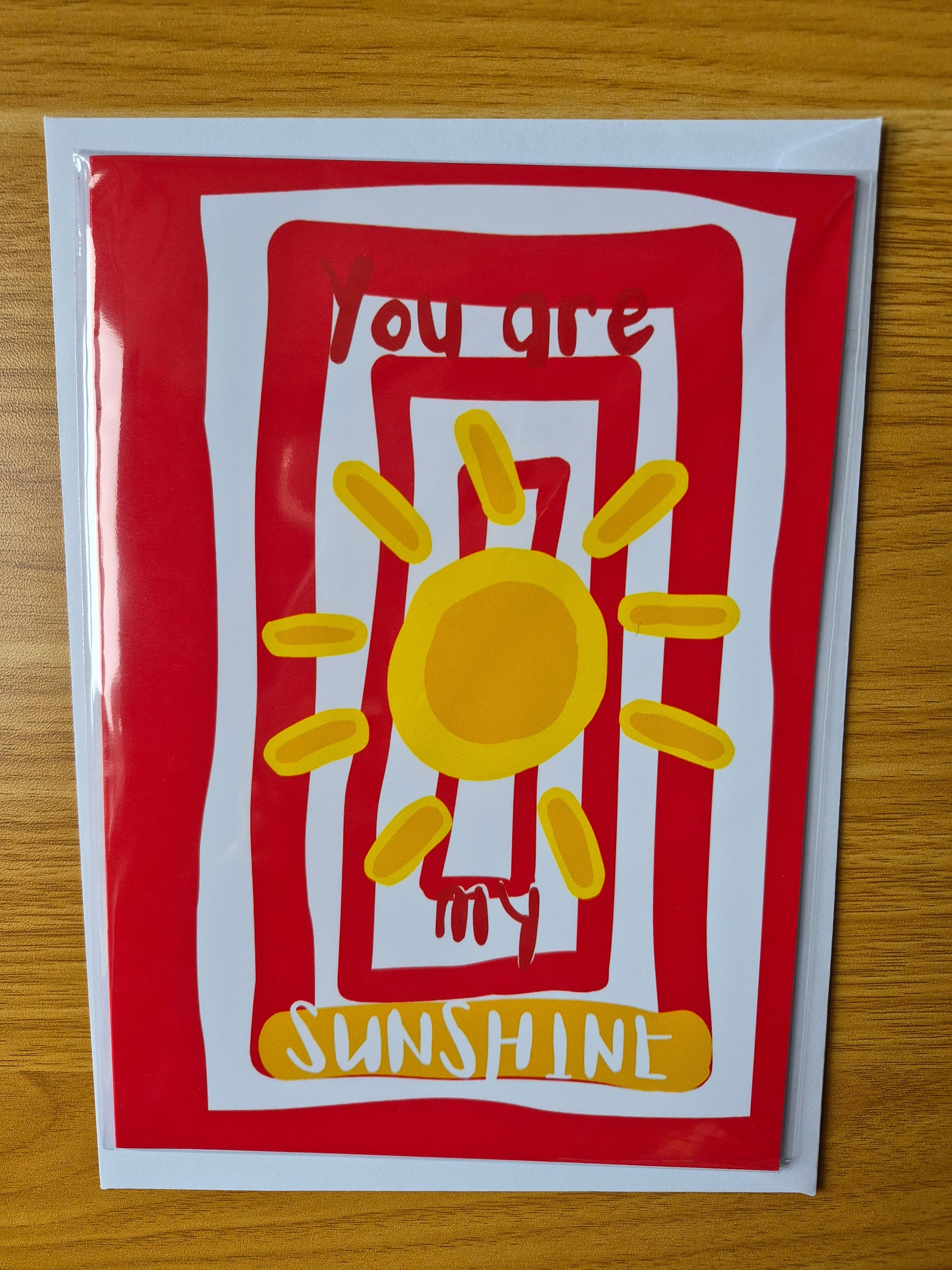 Card with a yellow sun design and red striped border on a wooden surface