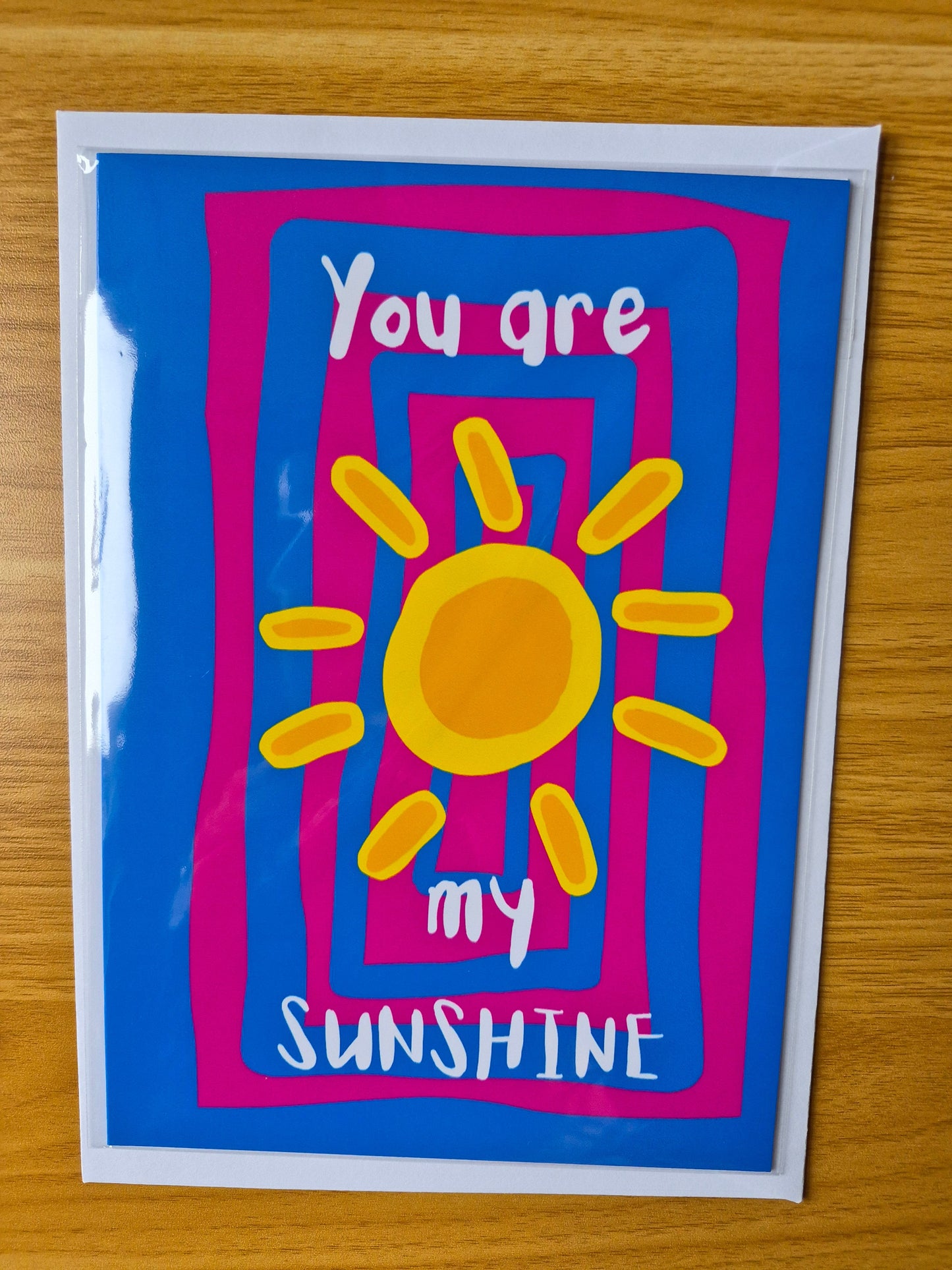 Pint and blue greetings card with a sun illustration and text 'You are my sunshine' on a wooden surface