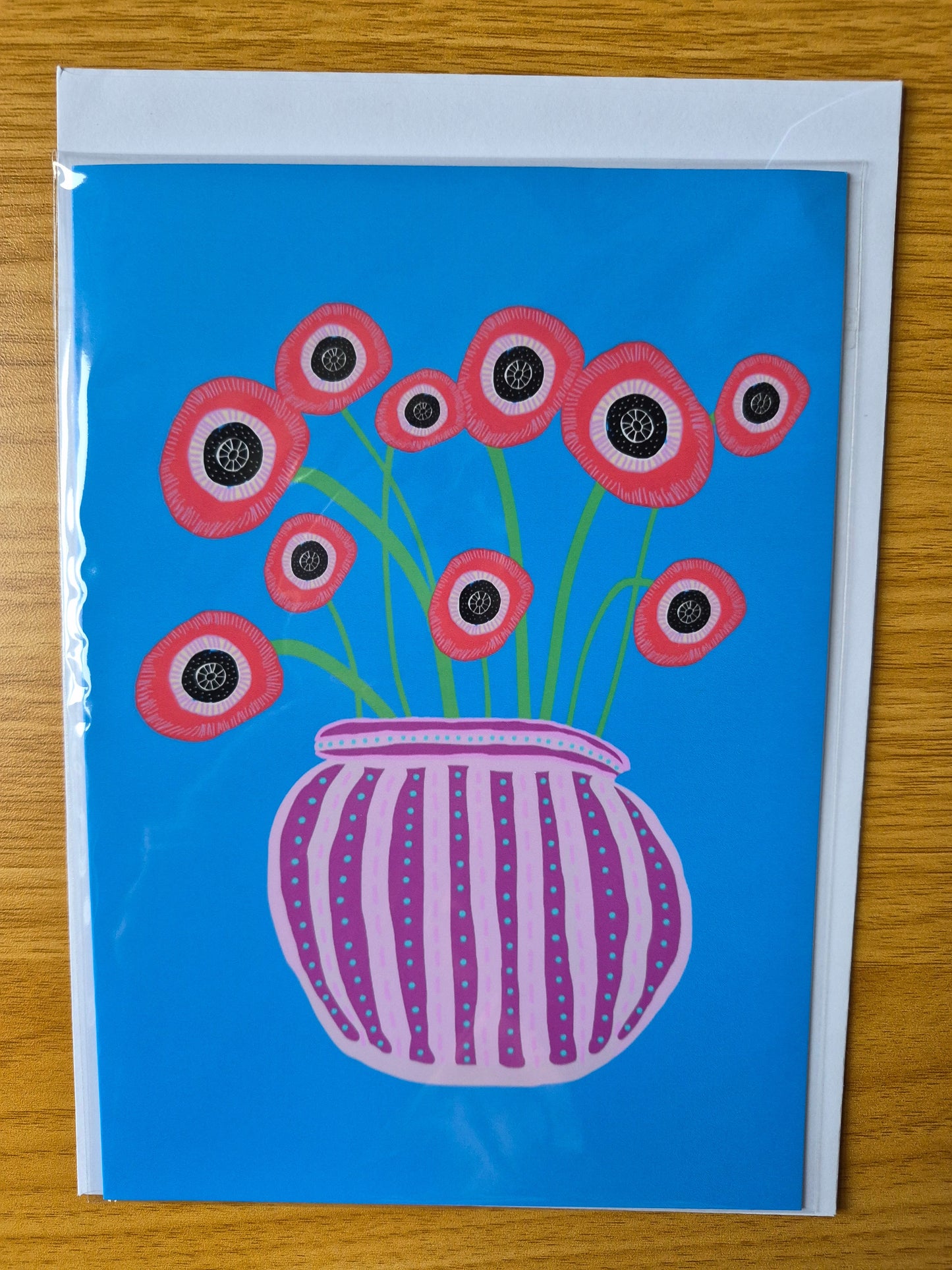 Greetings card featuring hand illustrated, abstract poppies in a purple stripy vase on a blue background.