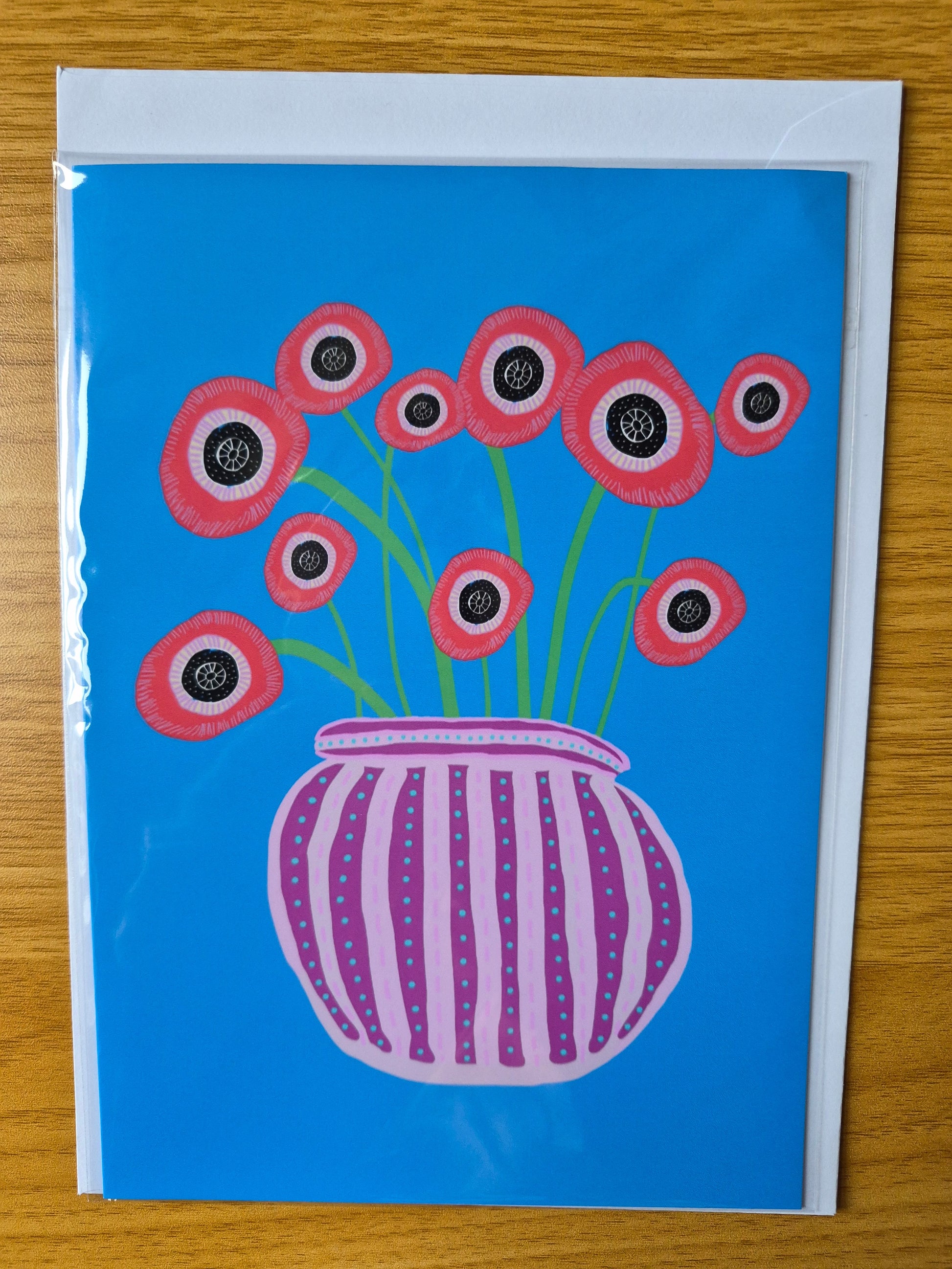 Greetings card featuring hand illustrated, abstract poppies in a purple stripy vase on a blue background.