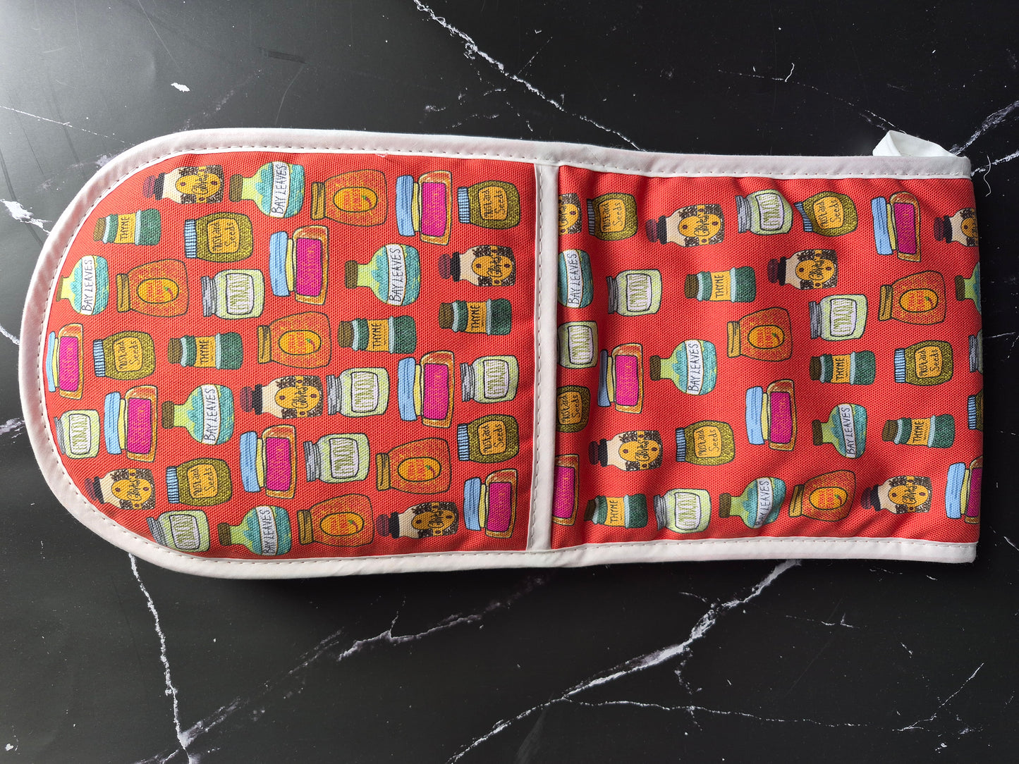 Red oven mitts with a spice jar design on a black marble worktop