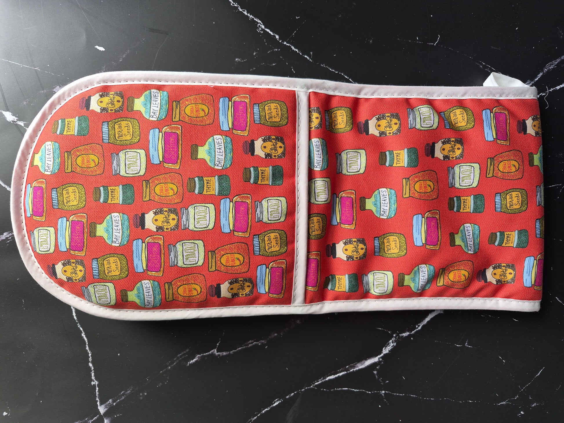 Red oven mitts with a spice jar design on a black marble worktop