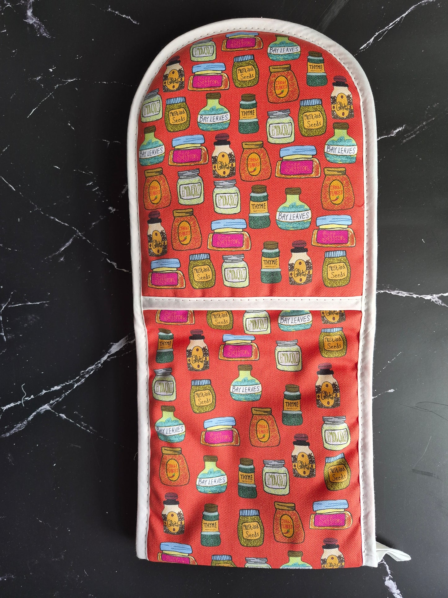 Red oven gloves with a hand-drawn spice jar print on a black worktop