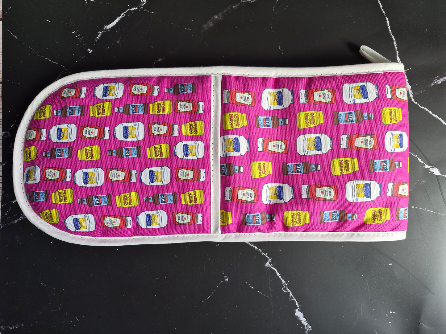 Hot pink oven mitts with a condiments print design on a black worktop