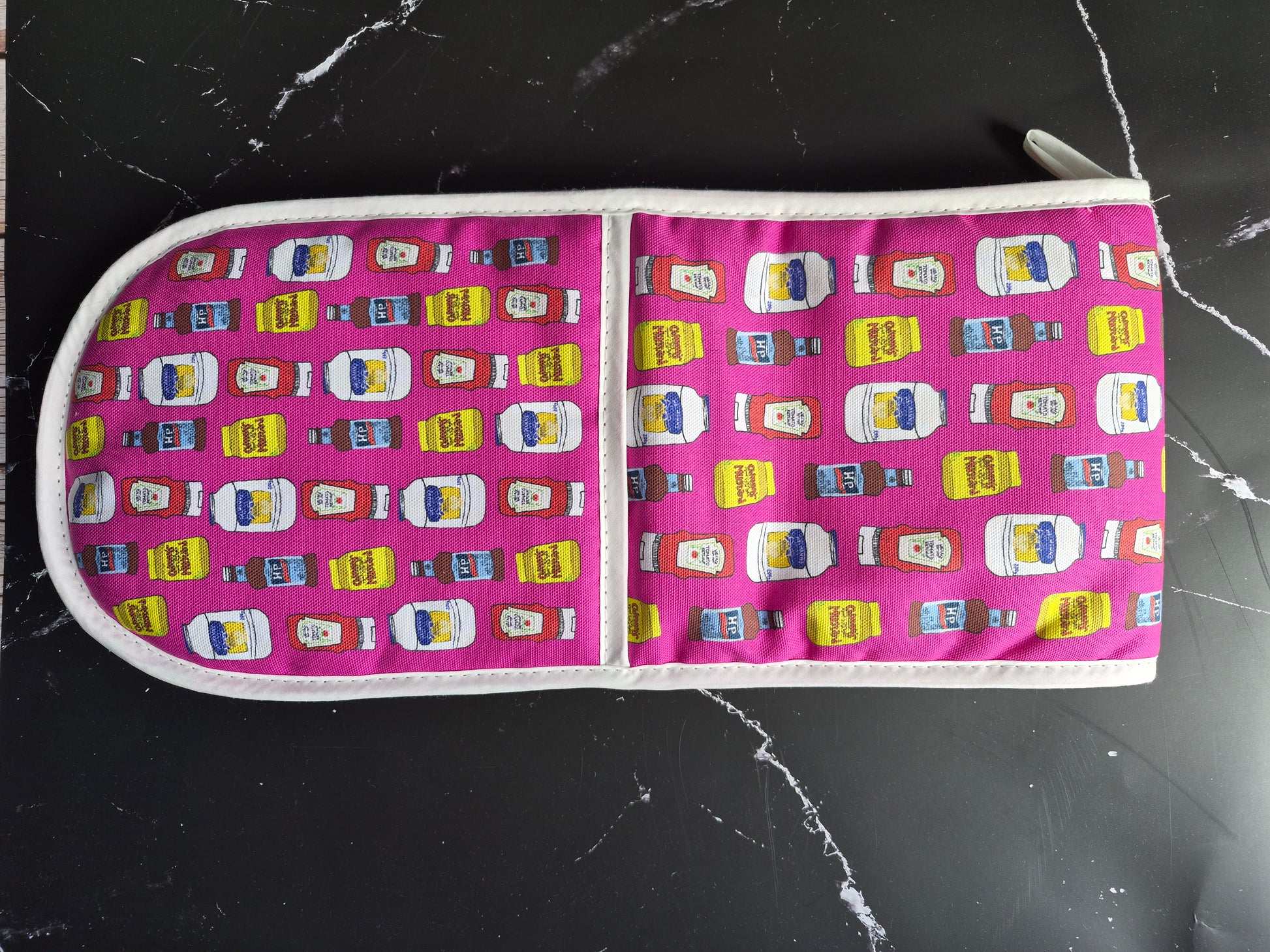 Hot pink oven mitts with a condiments print design on a black worktop