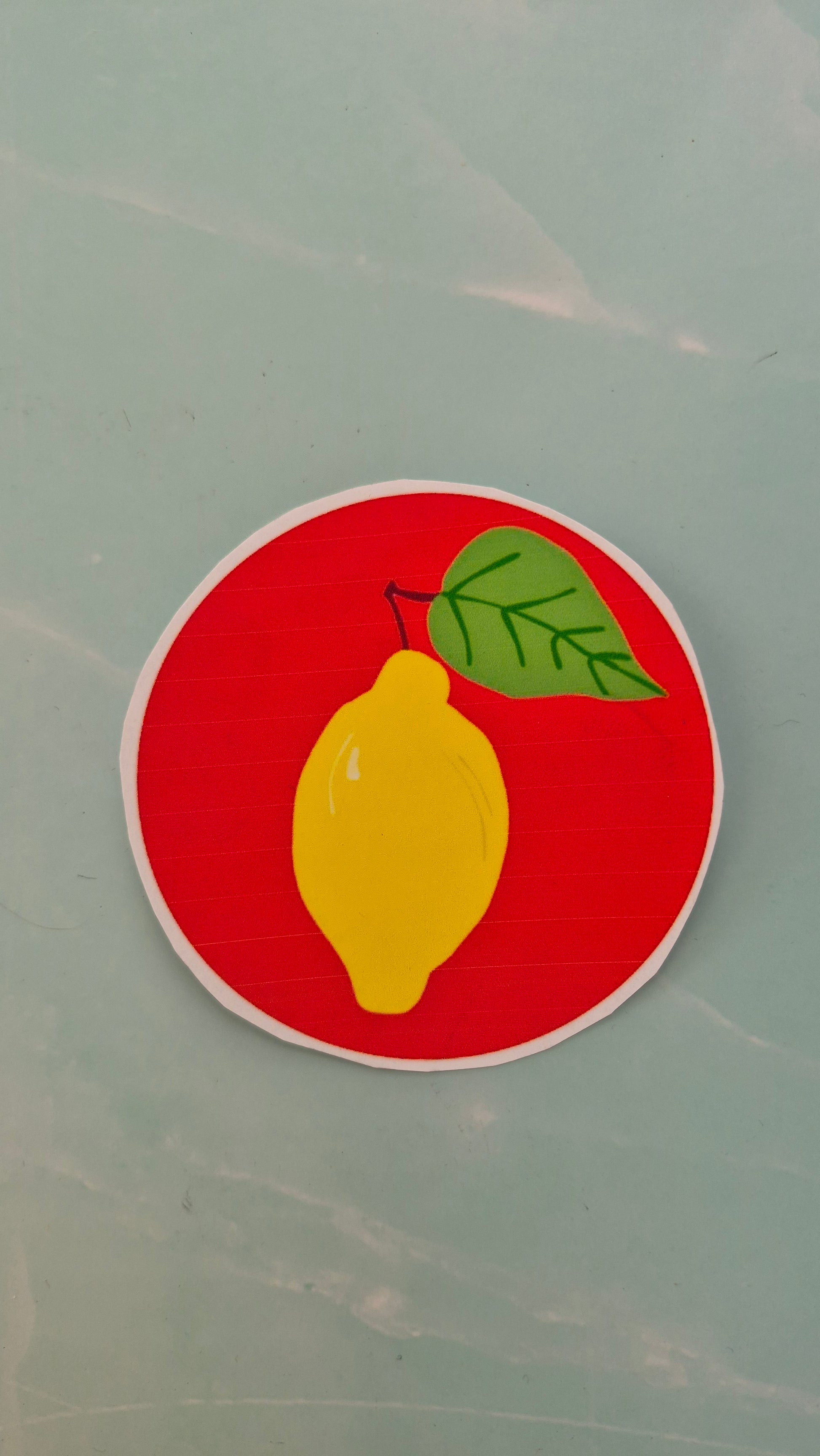 Vinyl sticker of a yellow lemon with a green leaf on a red circle against a light blue background