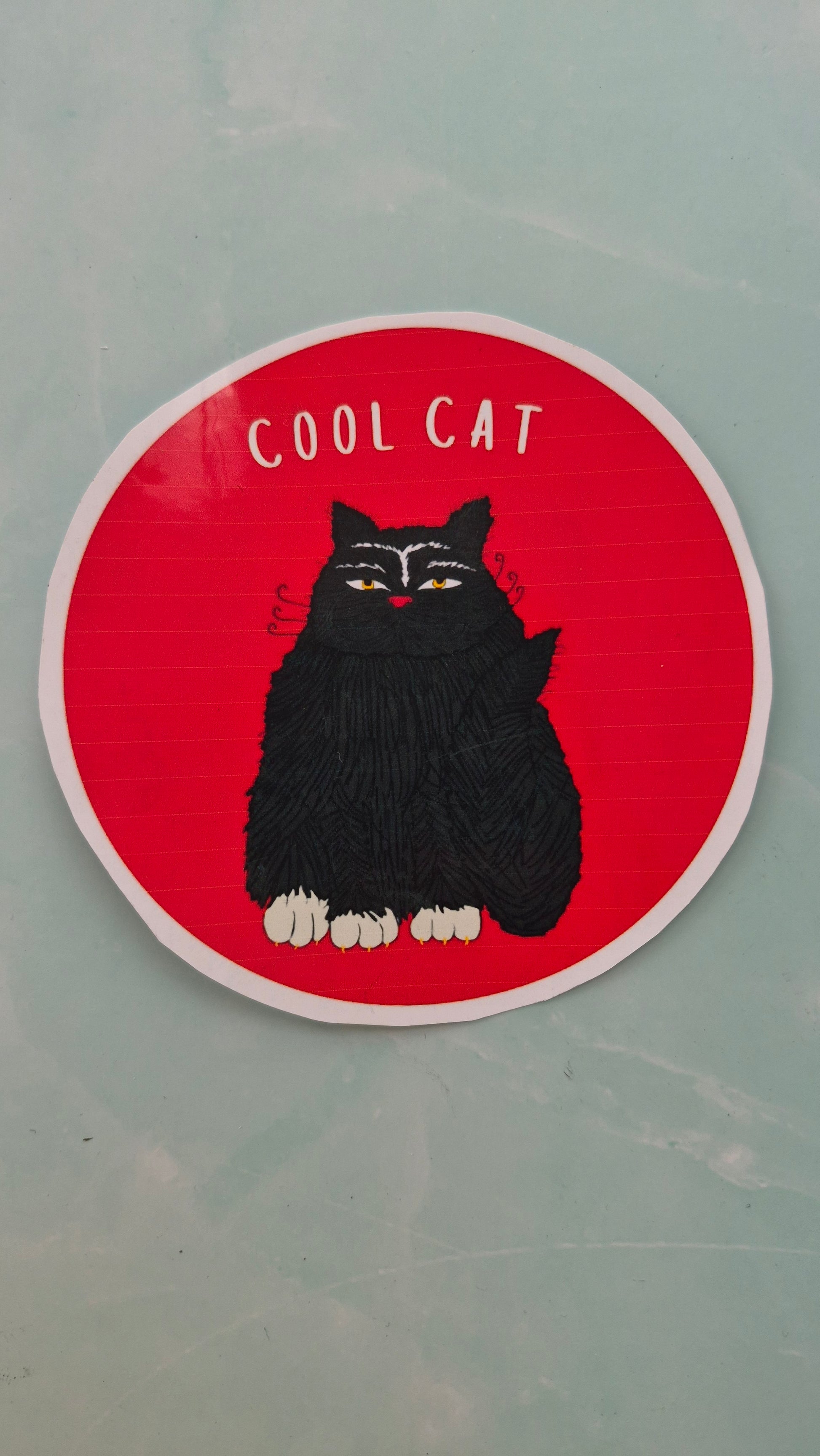 Circular red sticker with a black cat illustration and 'Cool Cat' text on a light blue marbled background