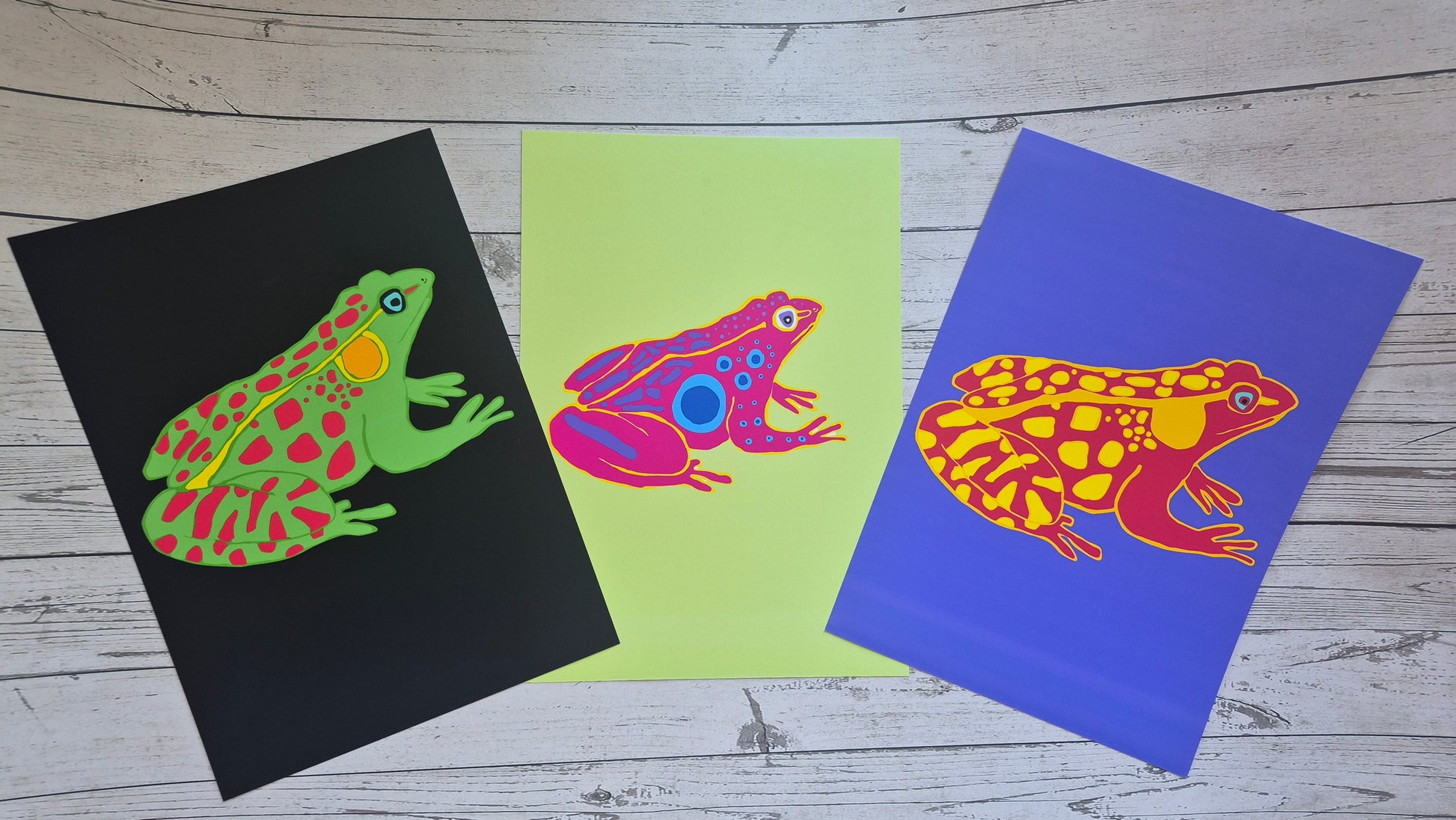 Three u frog print illustrations on black, green, and purple cards.