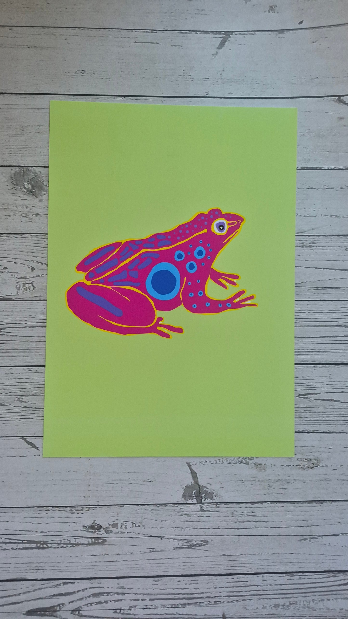 Colorful frog illustration on a green card with a wooden background