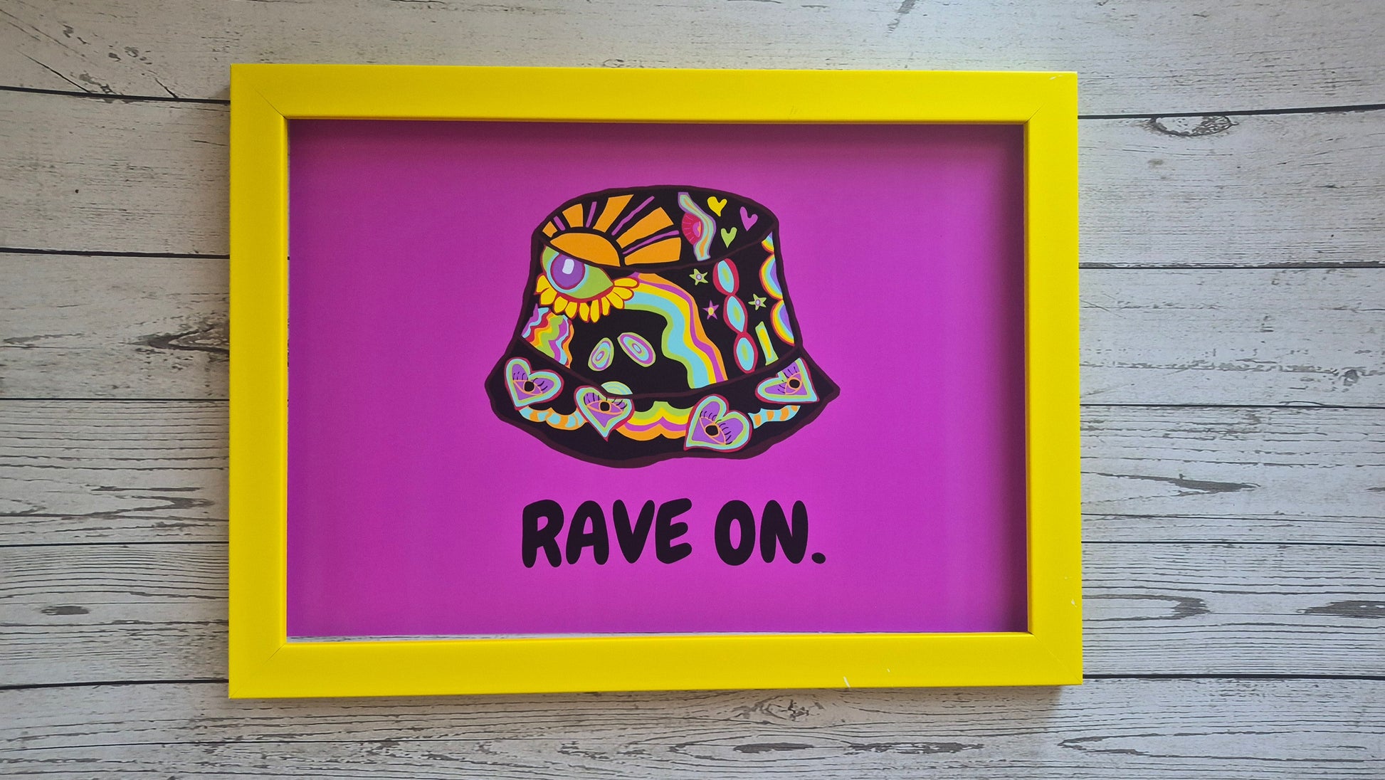 Framed artwork with a colourful bucket hat design and 'RAVE ON.' text on a pink/purple background.