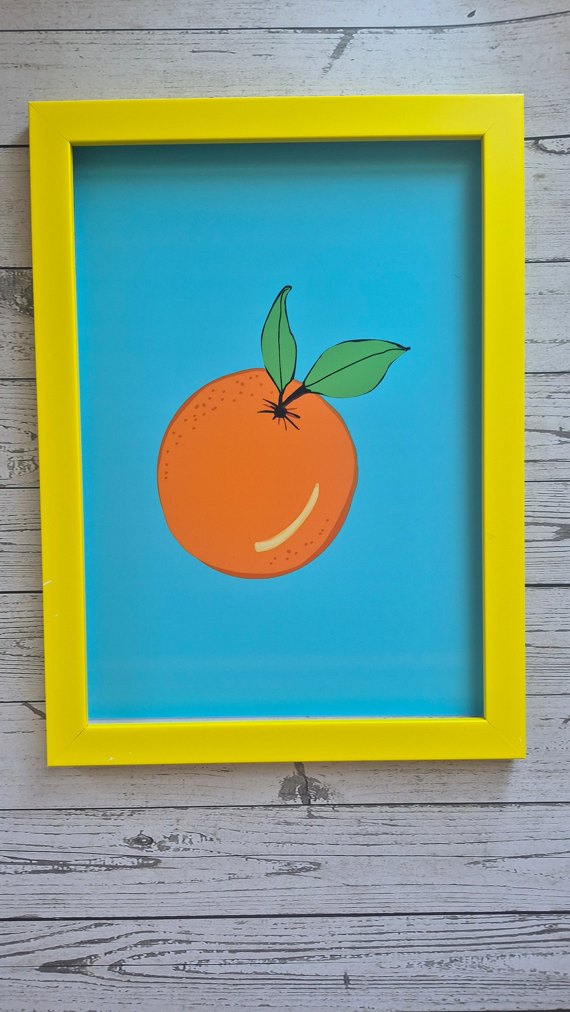 Yellow framed art print of an orange. A solid sky blue background. 