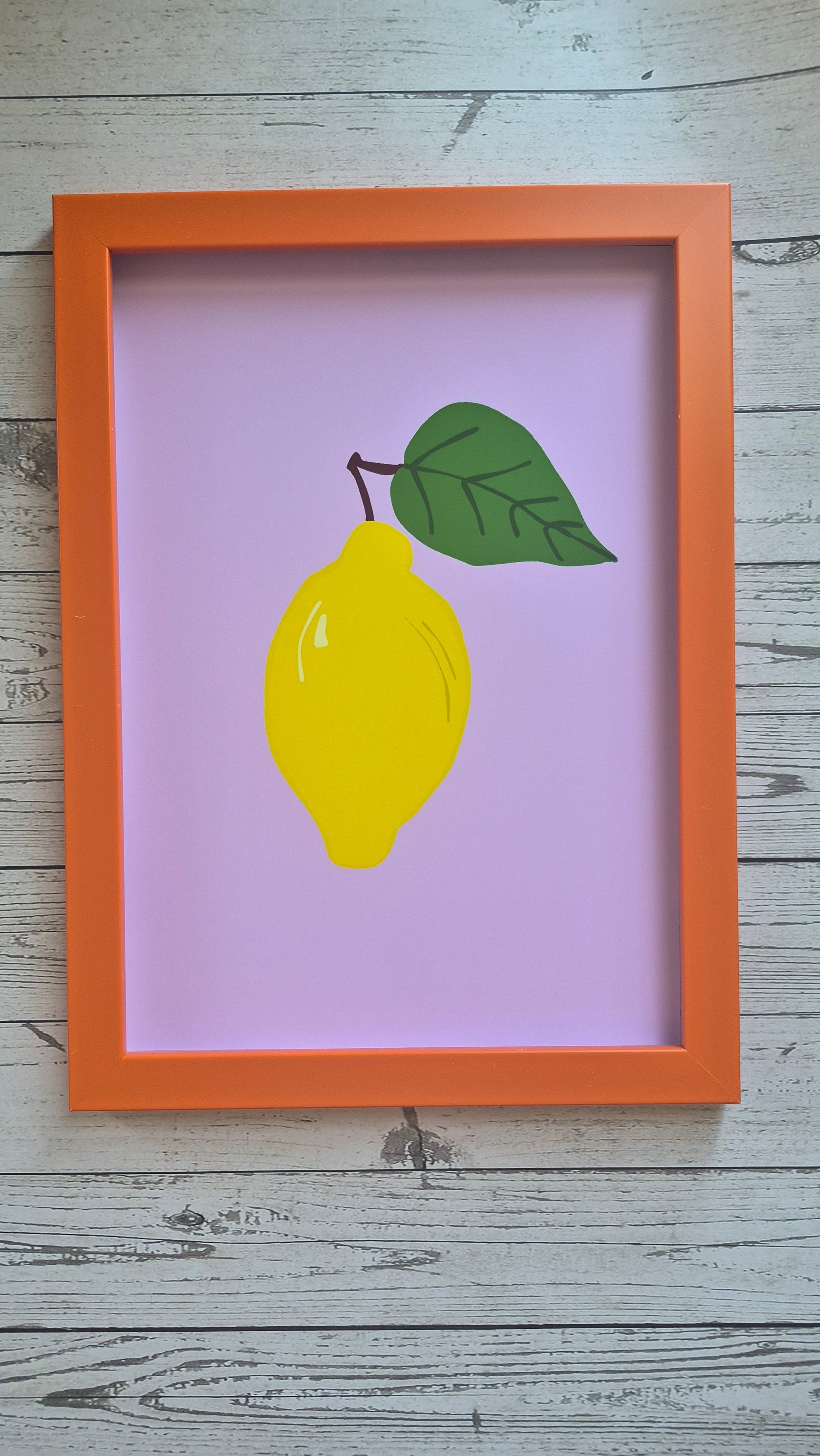 Framed illustration of a lemon with a leaf on a purple background in an orange frame. 