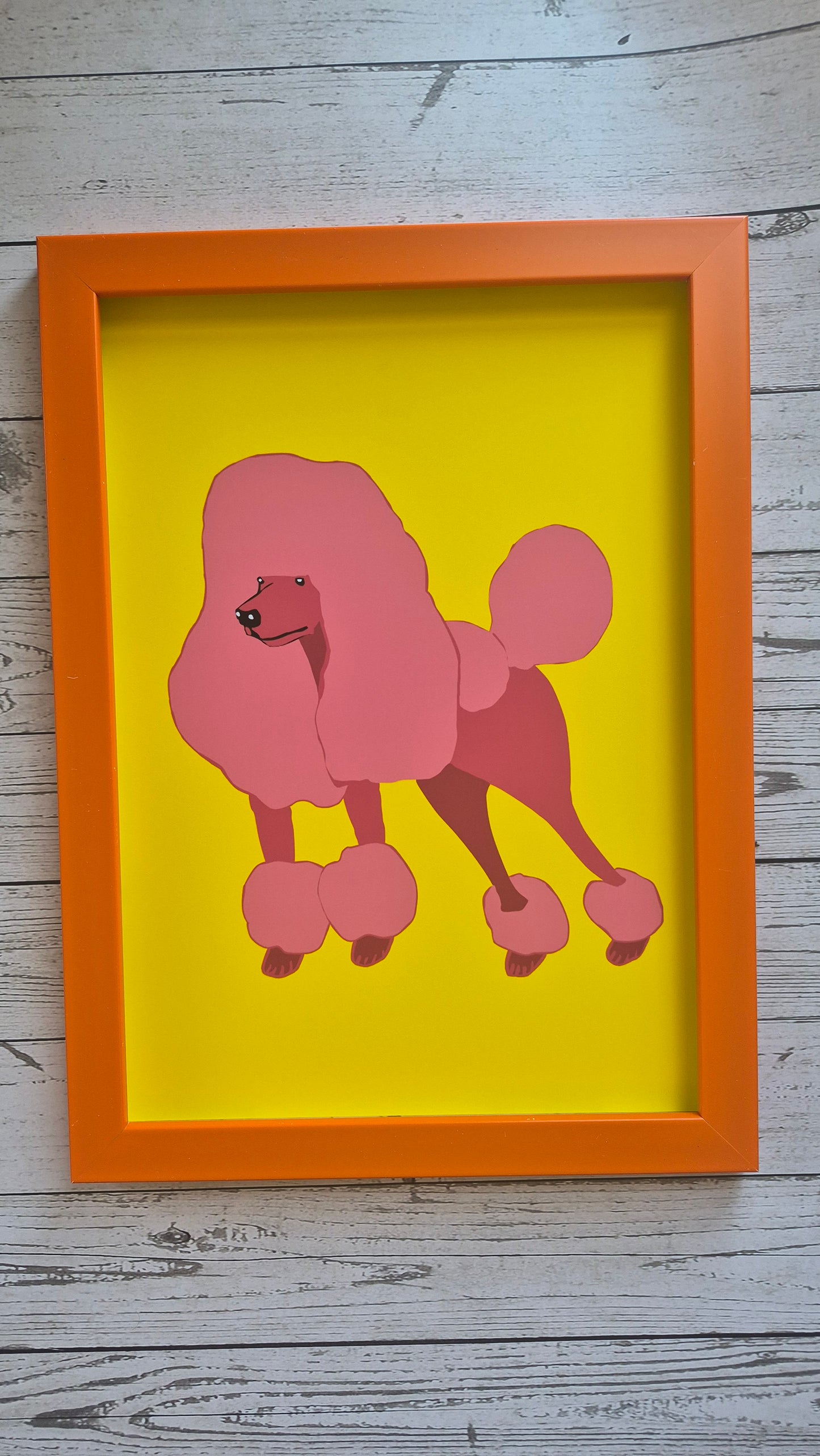 Framed artwork of a pink illustrated poodle design print on a solid yellow background in an orange frame.