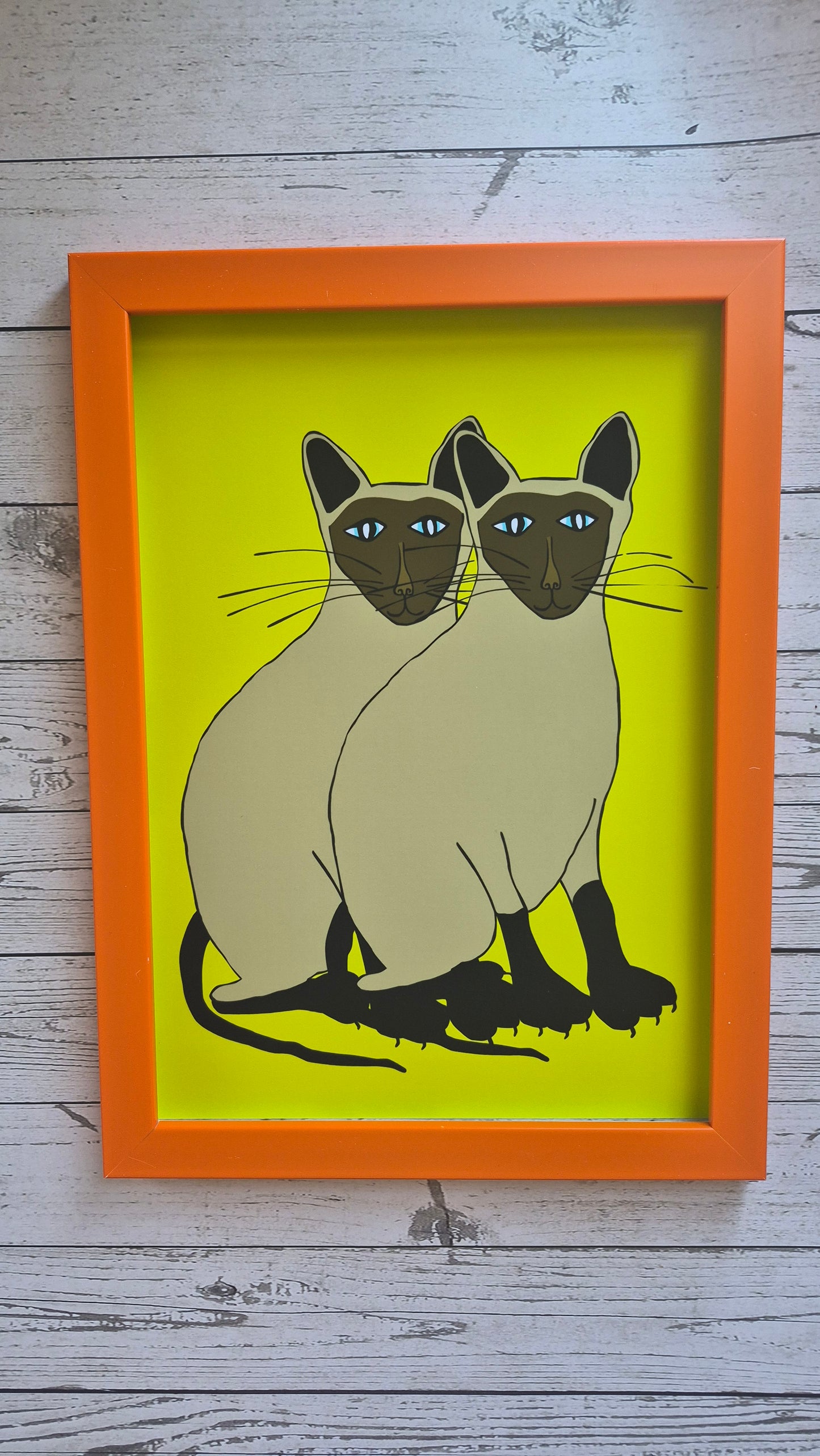 Framed illustration of a two Siamese cats on a lime green background. he frame is orange. 