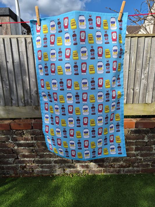Unique blue tea towel with hand drawn condiments print hanging on a washing line. 