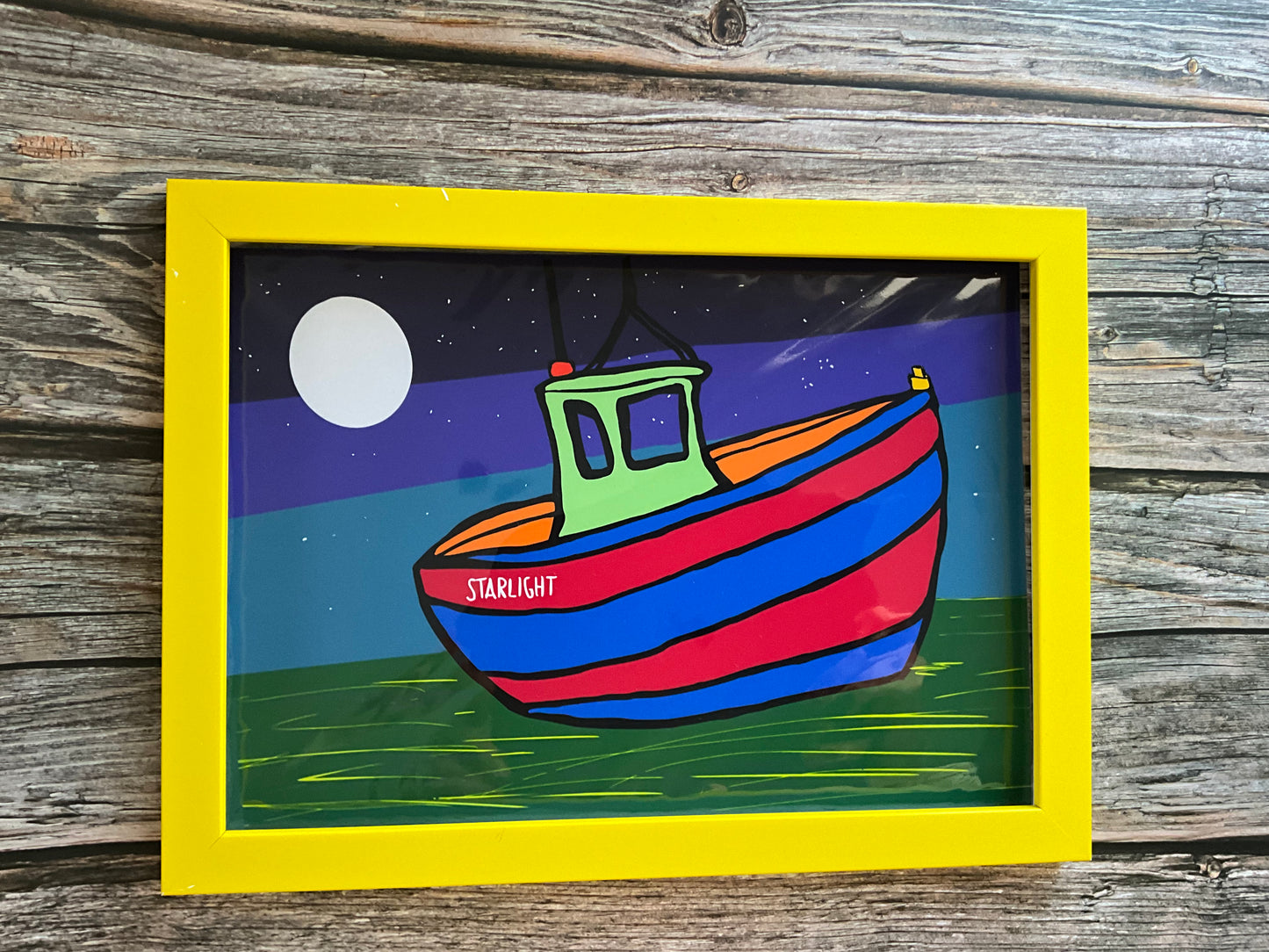 Colorful boat illustration with a yellow frame on a wooden surface