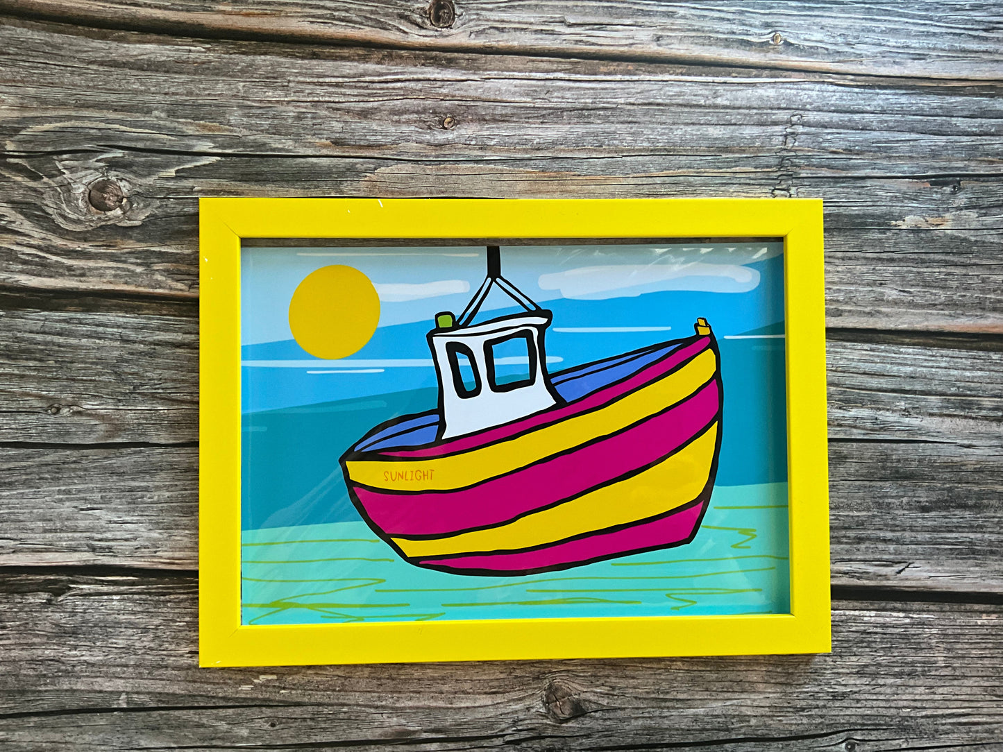 Colorful boat illustration in a yellow frame on a wooden background