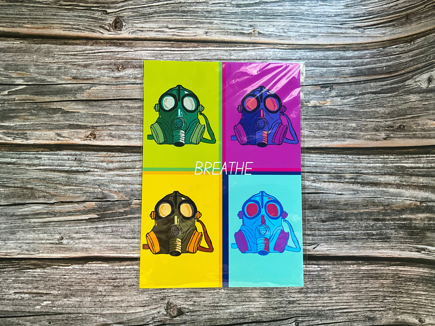 Retro art print. Four gas mask illustrations on a colour block background with 'BREATHE' text, placed on a wooden surface.