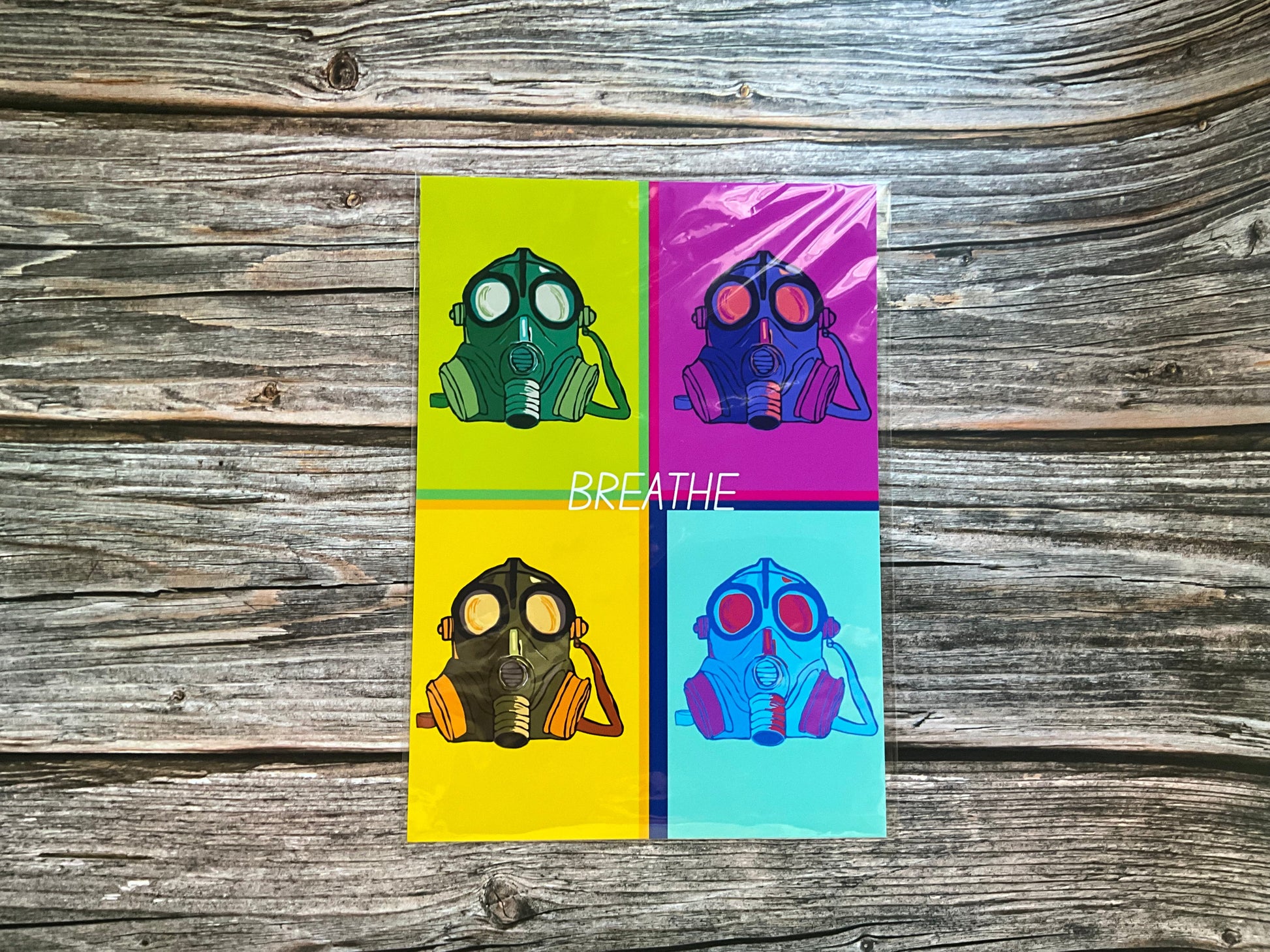Retro art print. Four gas mask illustrations on a colour block background with 'BREATHE' text, placed on a wooden surface.
