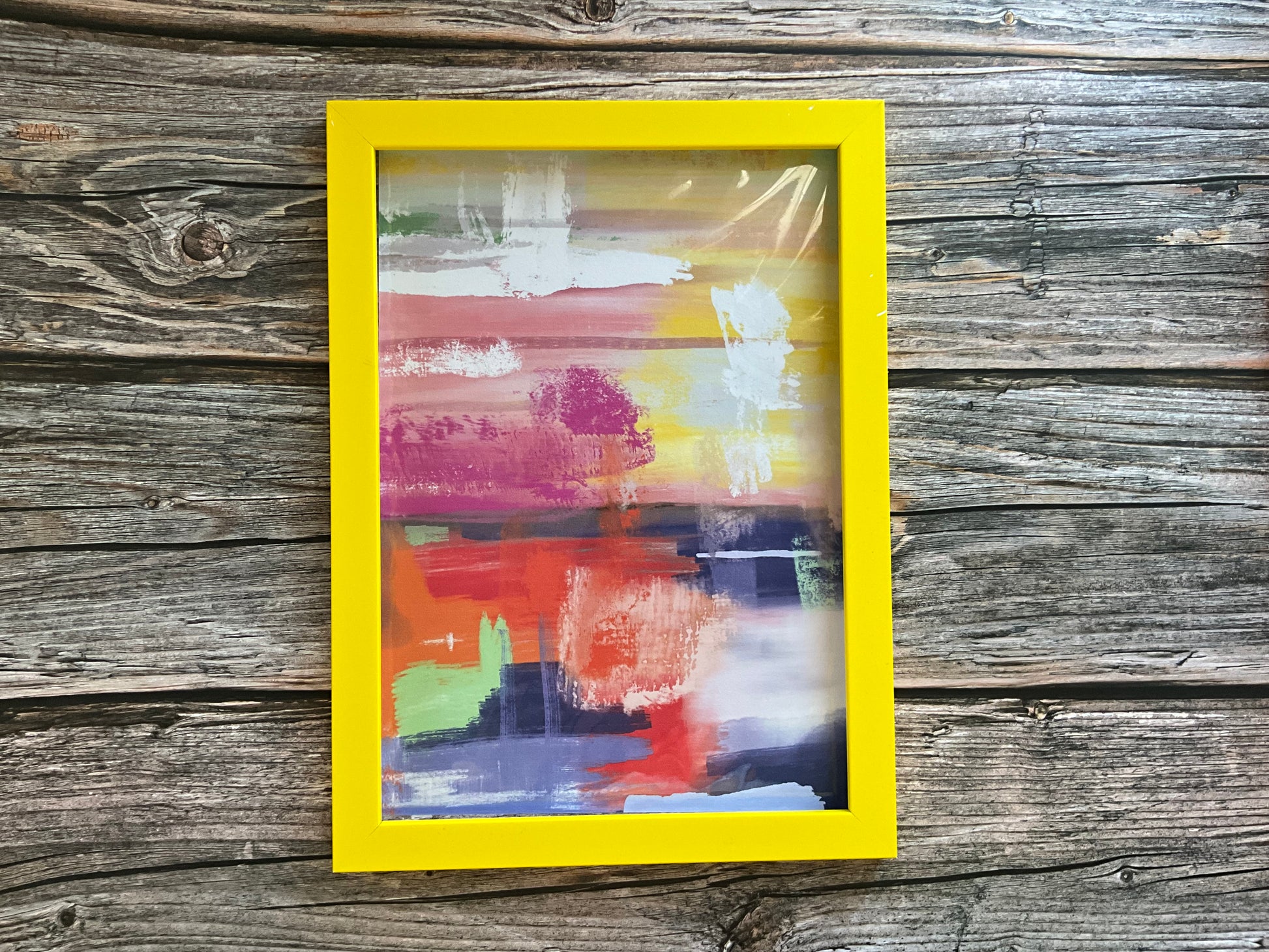 Bright abstract landscape print in a yellow frame on a wooden surface