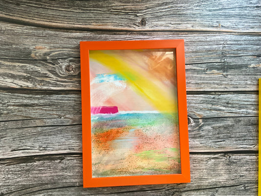 Framed abstract artwork with an orange border on a wooden surface
