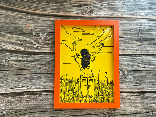 Art print of a girl in a meadow field raising her hands to the sky. The print is framed in an orange frame and has a bright yellow background. 