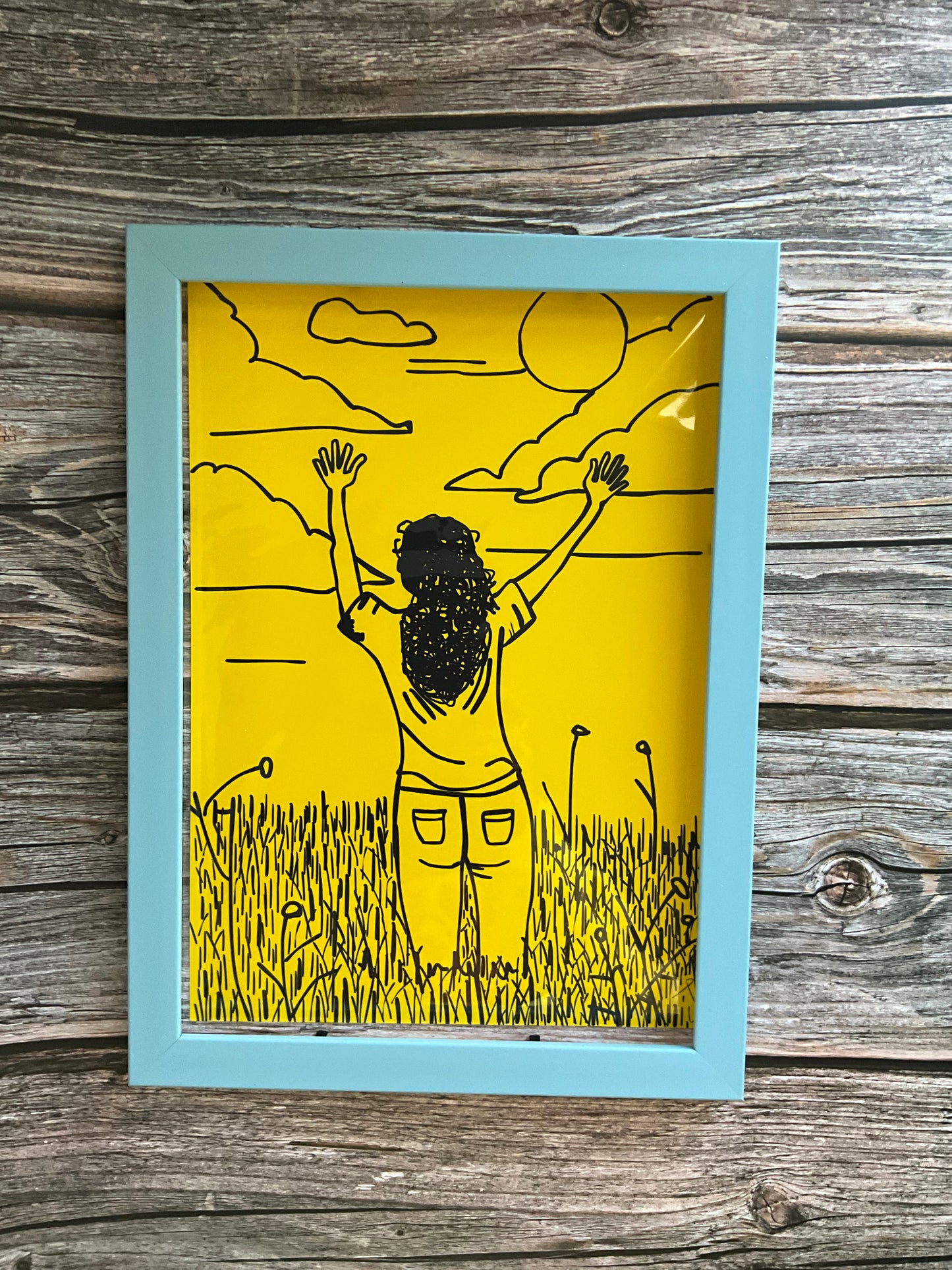 Art print of a girl in a meadow field raising her hands to the sky. The print is framed in an blue frame and has a bright yellow background. 