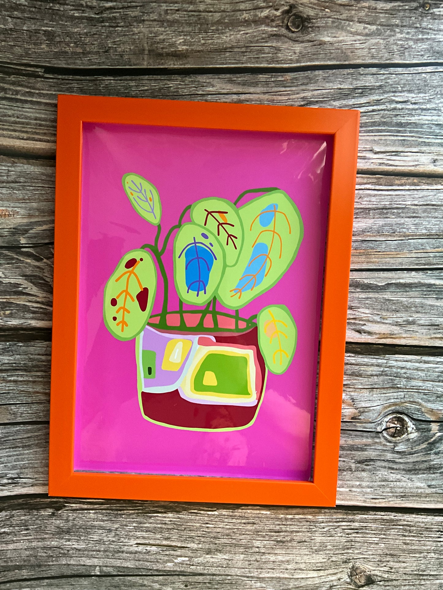 Framed artwork with colorful abstract  pot plant design on a wooden surface