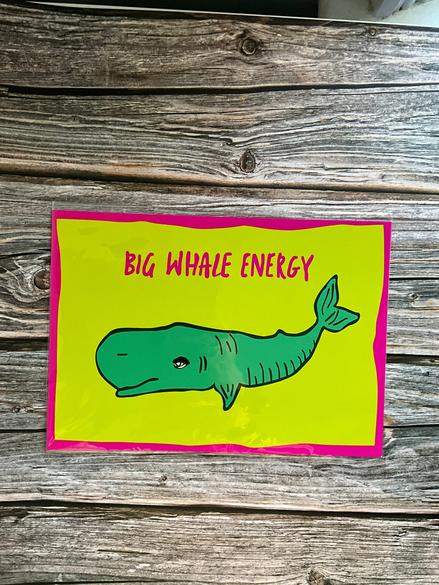Card with a green whale illustration and 'Big Whale Energy' text and a pink border, placed on wooden surface.