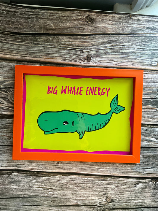 Framed artwork with a green whale illustration and 'BIG WHALE ENERGY' text on a wooden surface.