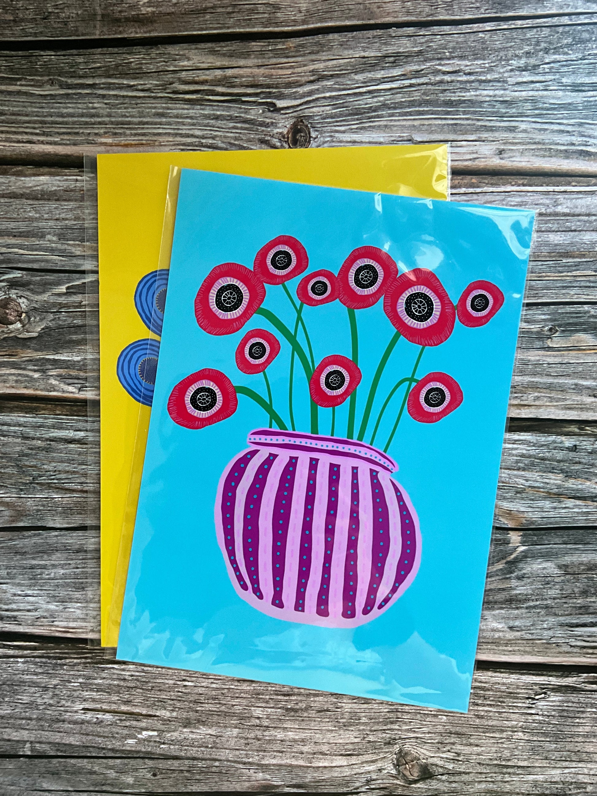 Abstract red poppy flower vase art print design with a blue background, on a wooden surface.