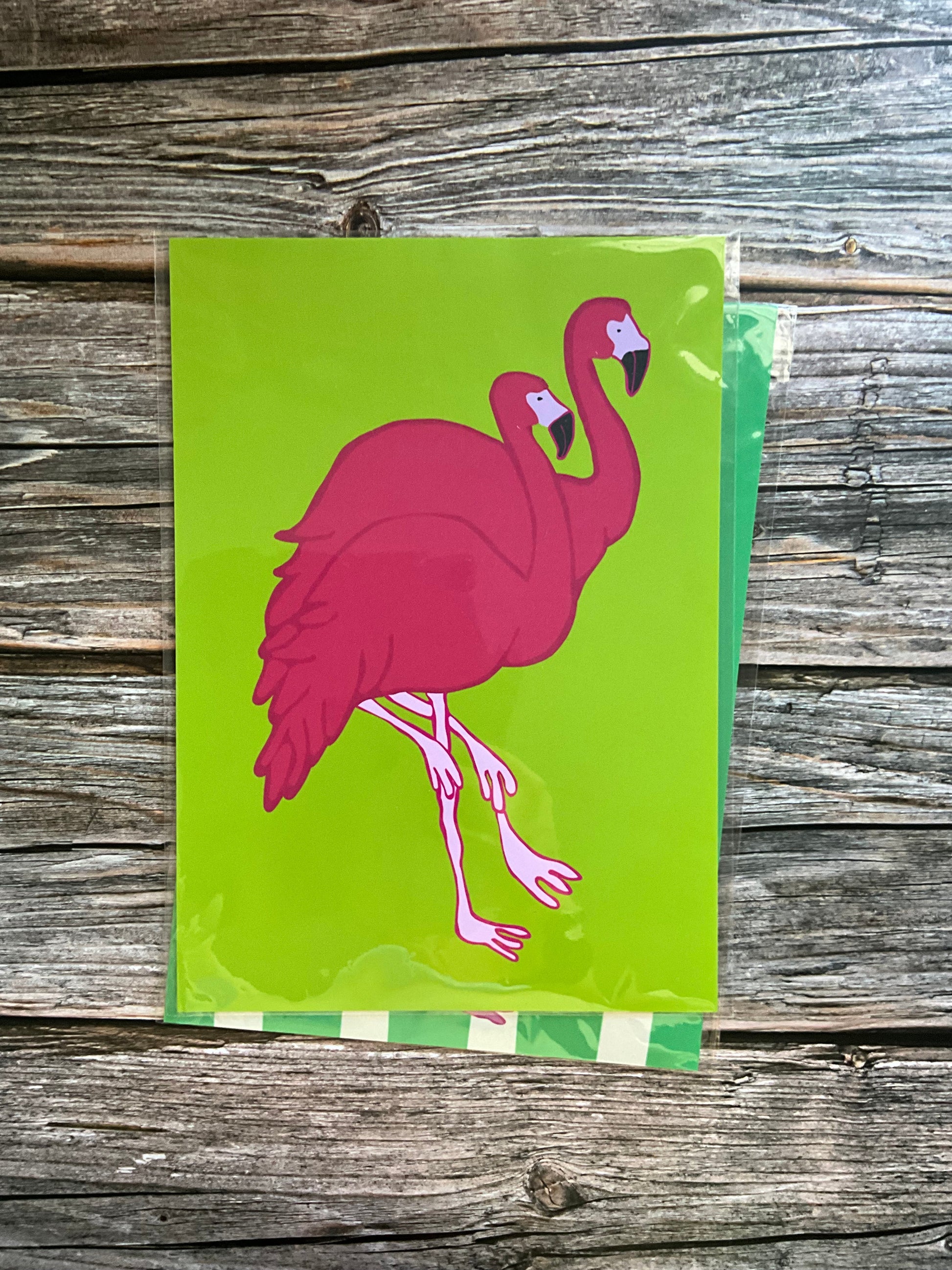 Art print with a pink flamingo design on a green background, placed on a wooden surface.