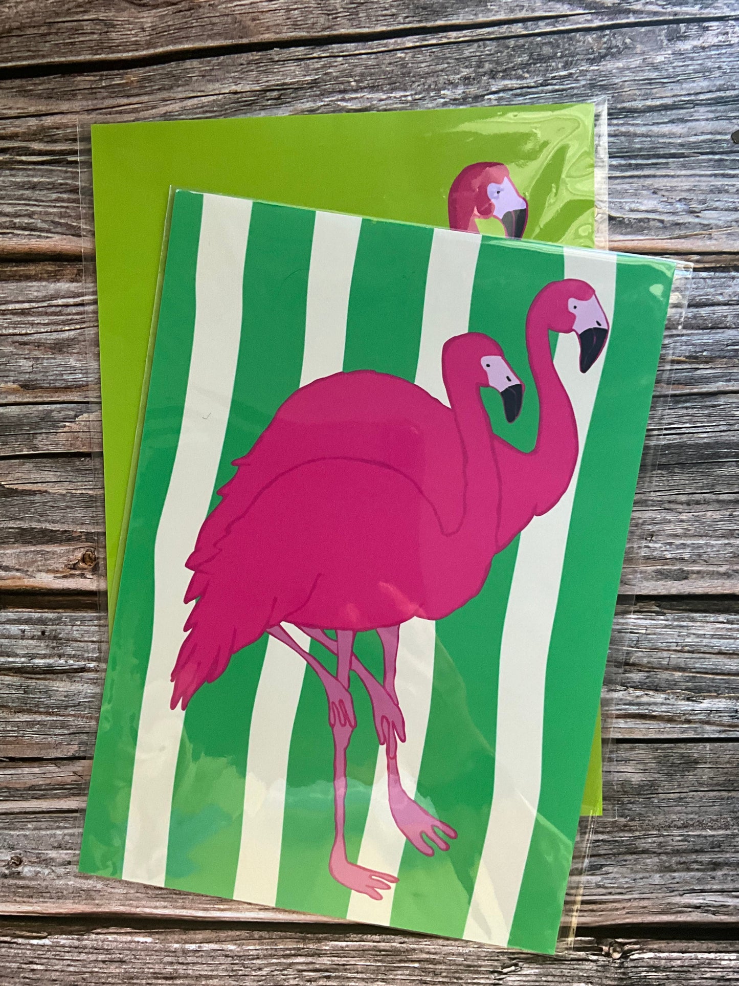 Art print with a pink flamingo on green and white striped background, placed on a wooden surface.