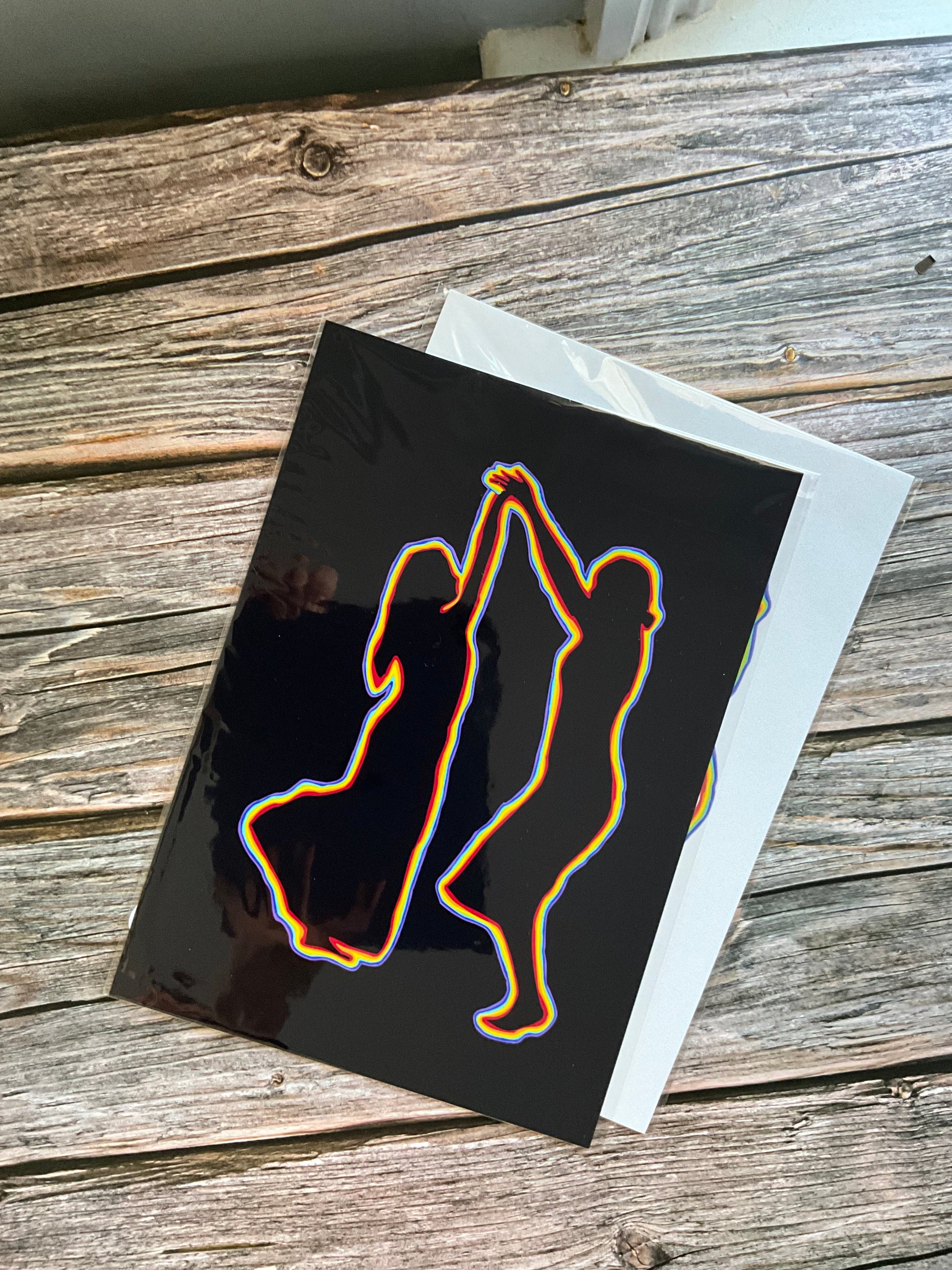 An art print of the outline of two women dancing in rainbow colours on a black background