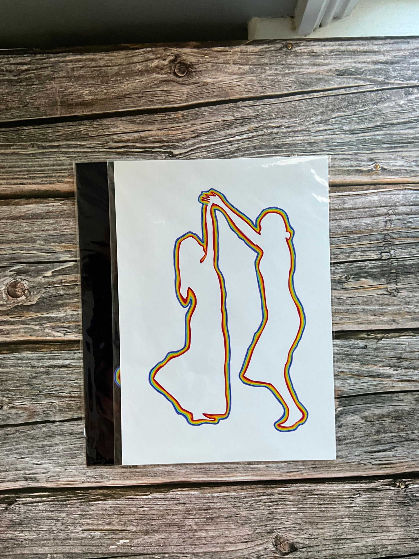 An art print of the outline of two women dancing in rainbow colours on a white background