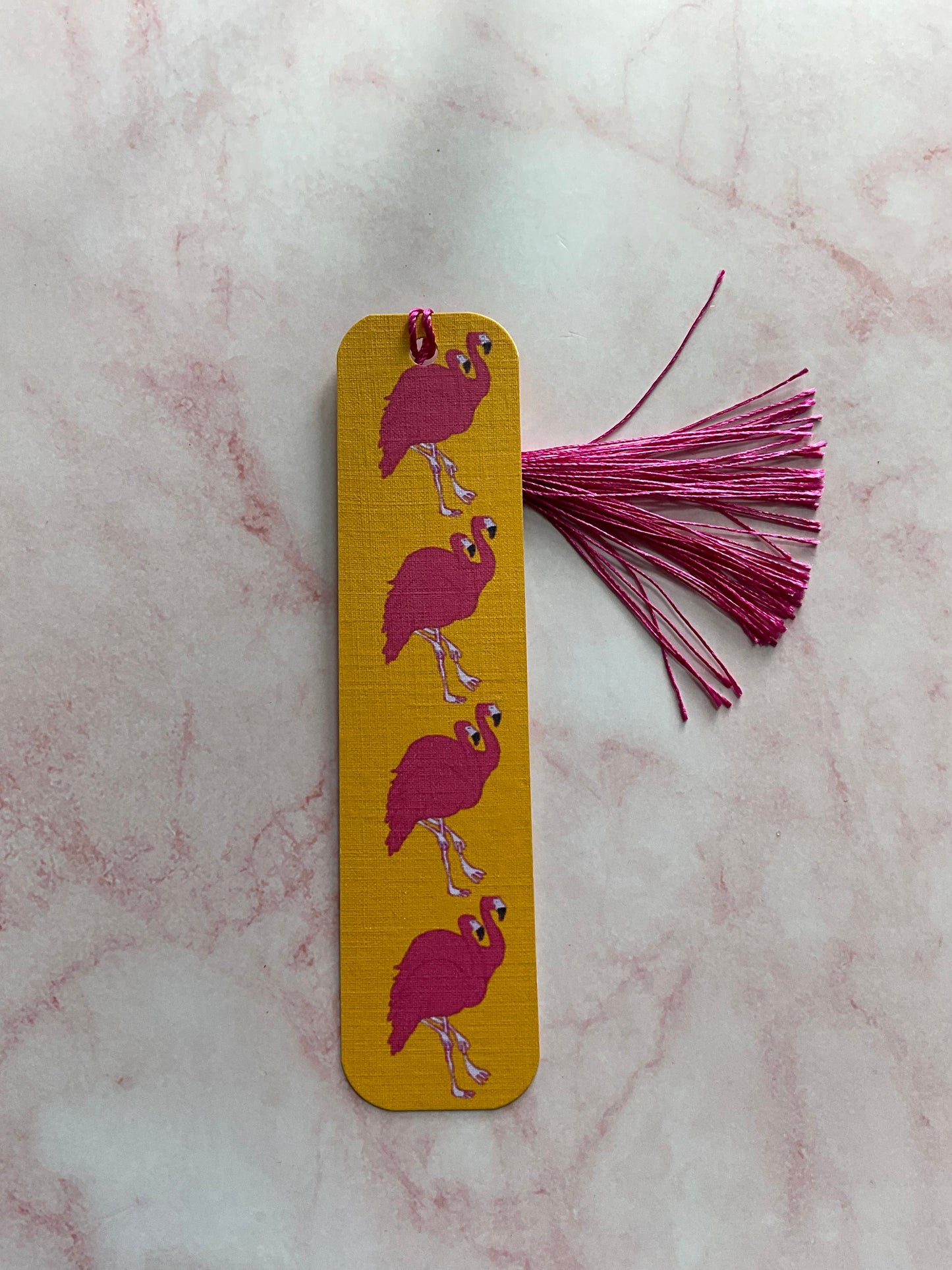 Decorative bookmark with pink birds design on an orange background, placed on a marble surface.