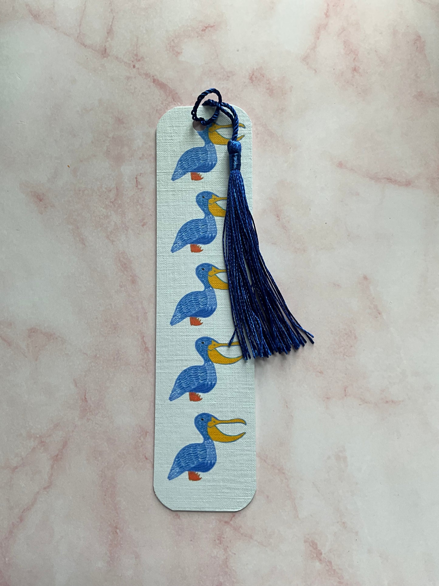 Pelican print bookmark with blue tassel on a pink marble background