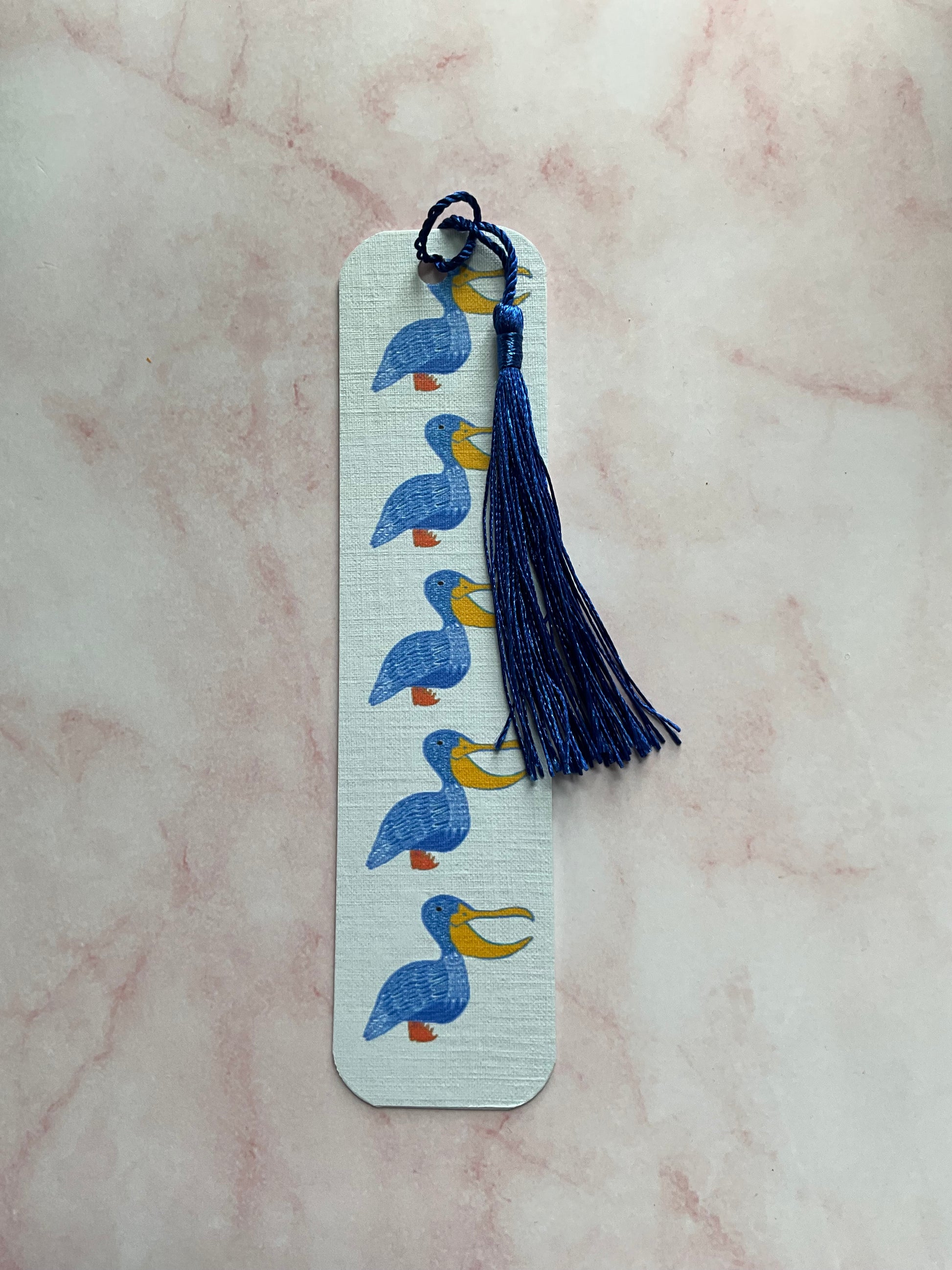 Pelican print bookmark with blue tassel on a pink marble background