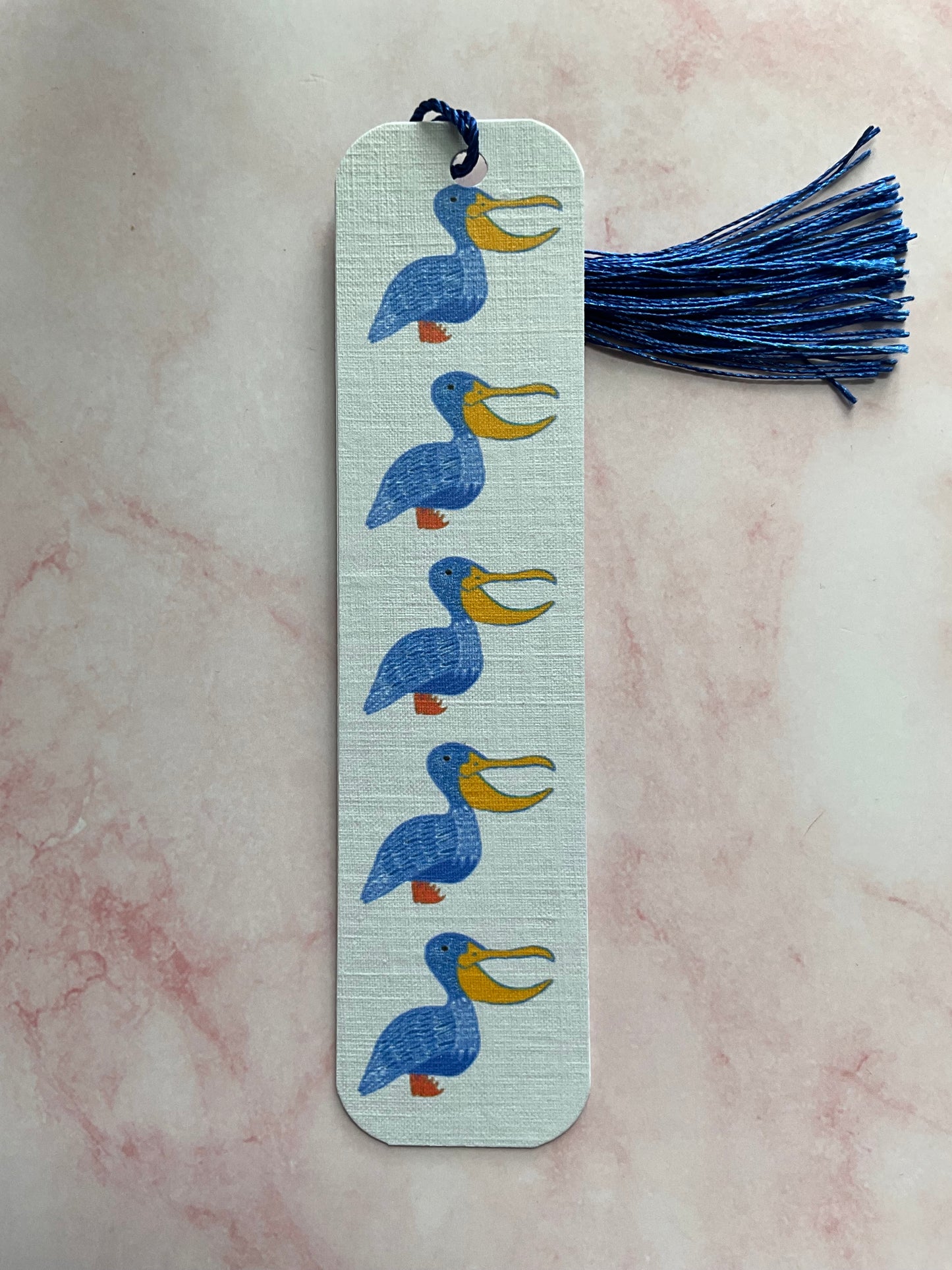 Pelican print bookmark with blue bird illustrations on a pink marble surface