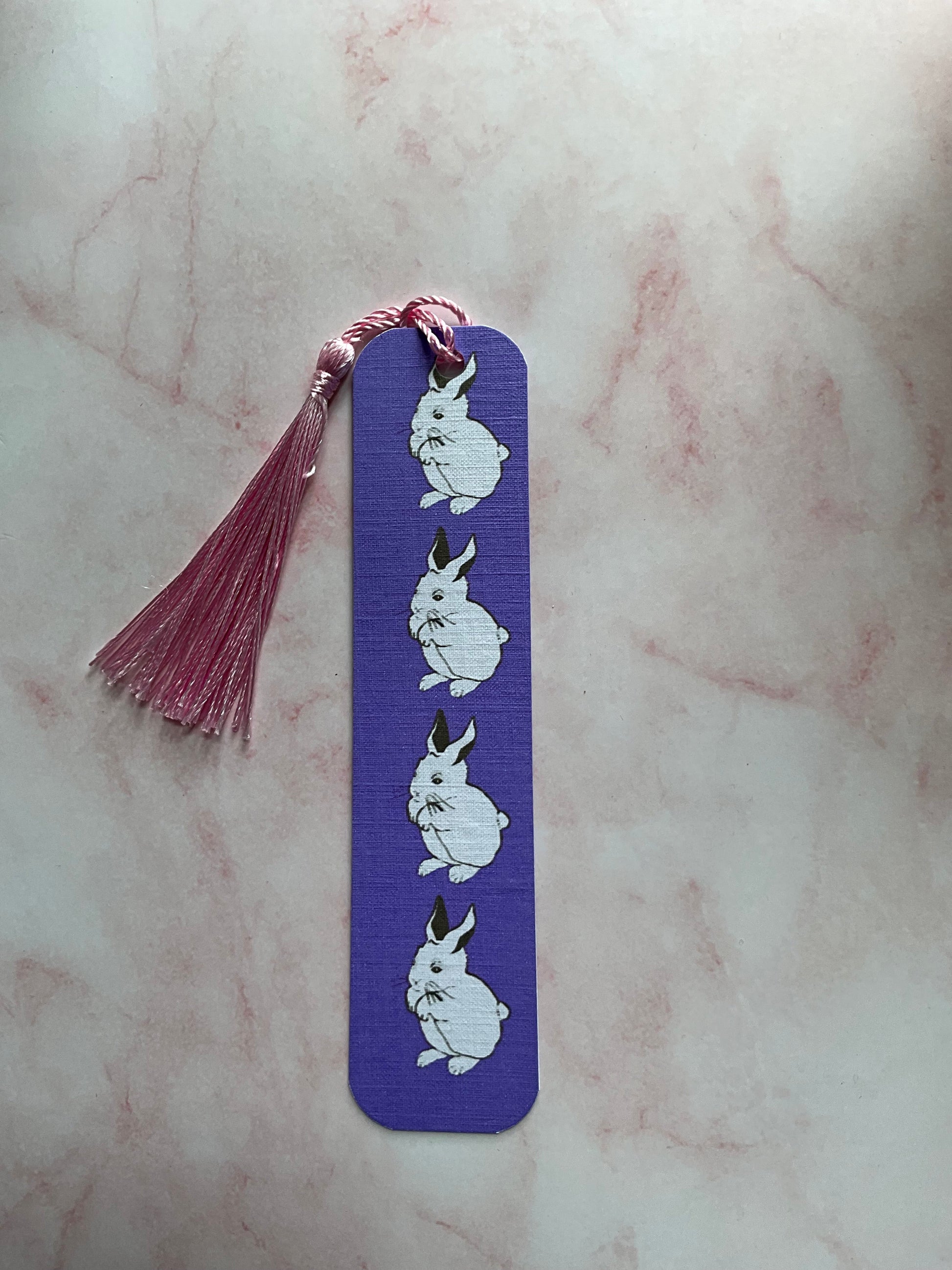 Purple bookmark with white bunny illustrations and a tassel on a marbled surface
