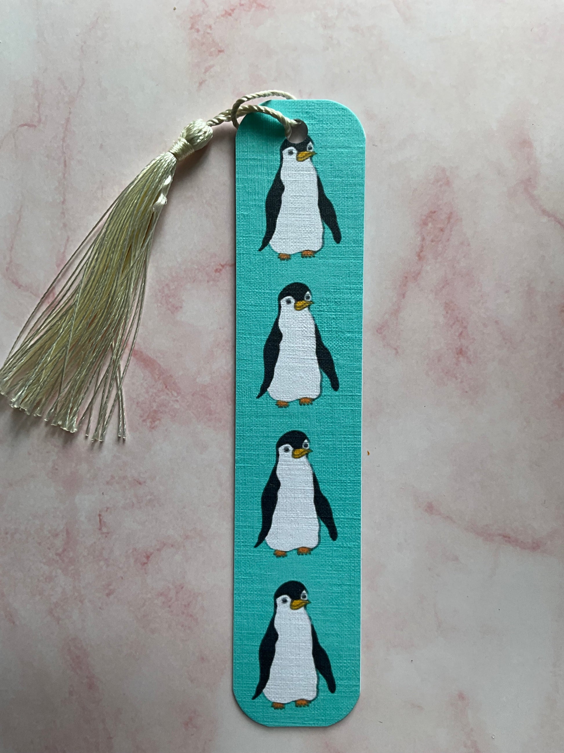 Bookmark with penguin design and tassel on a pink marble background