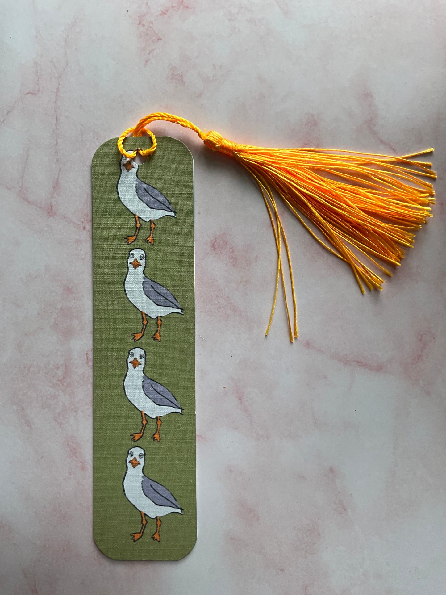 Green bookmark with bird design and yellow tassel on a marble surface