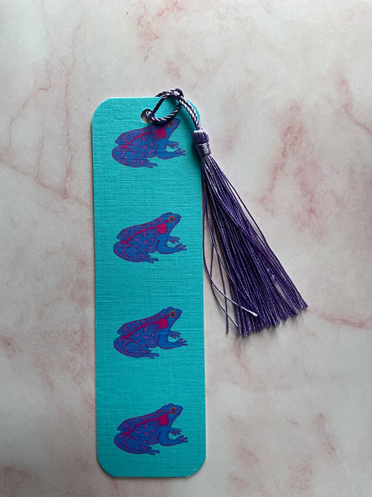 Blue bookmark with purple frog design and purple tassel on a pink marble background
