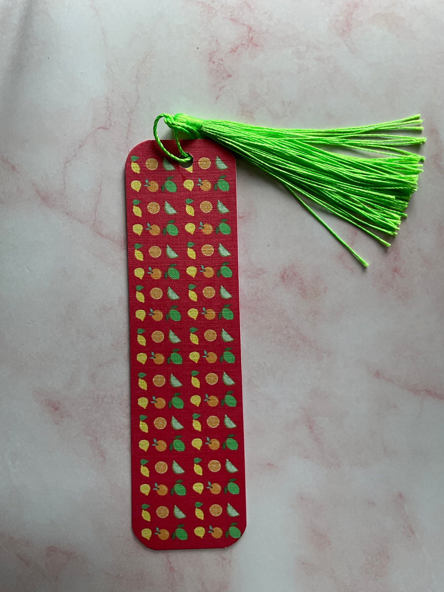 Red bookmark with fruit pattern and green tassel on a light pink surface